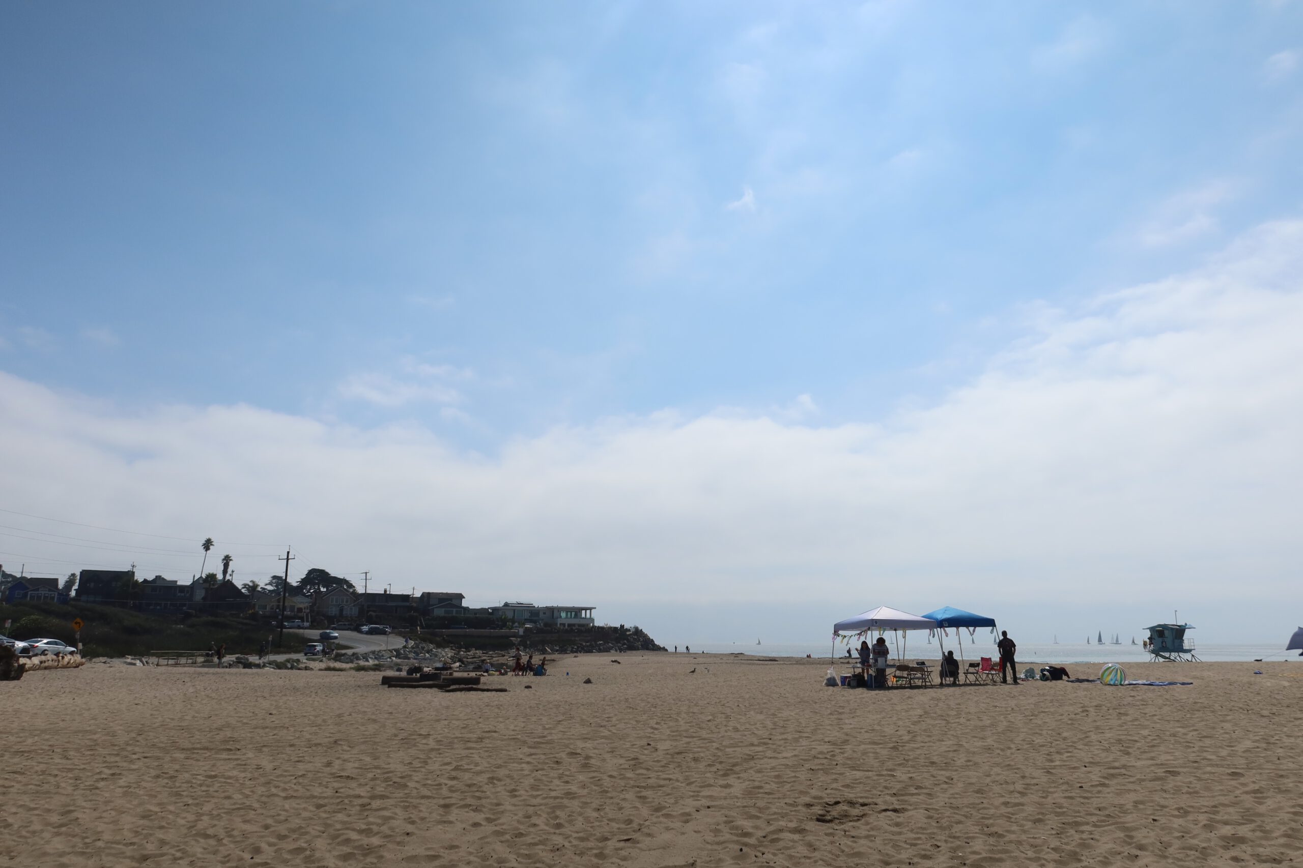Wide sandy beach at Twin Lakes State Beach in Santa Cruz, California with people relaxing under sun canopies and a calm Pacific Ocean in the background