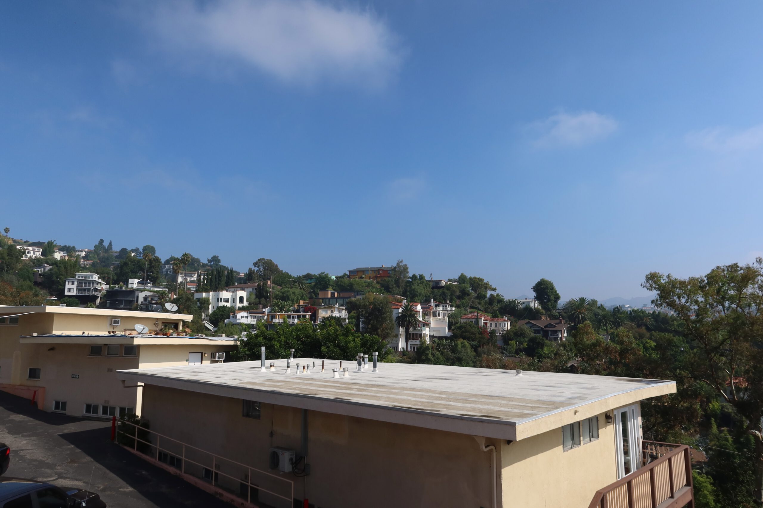 View over residential homes in the Hollywood Hills with trees, hillside houses, and a clear blue sky, photographed from an elevated hotel location.