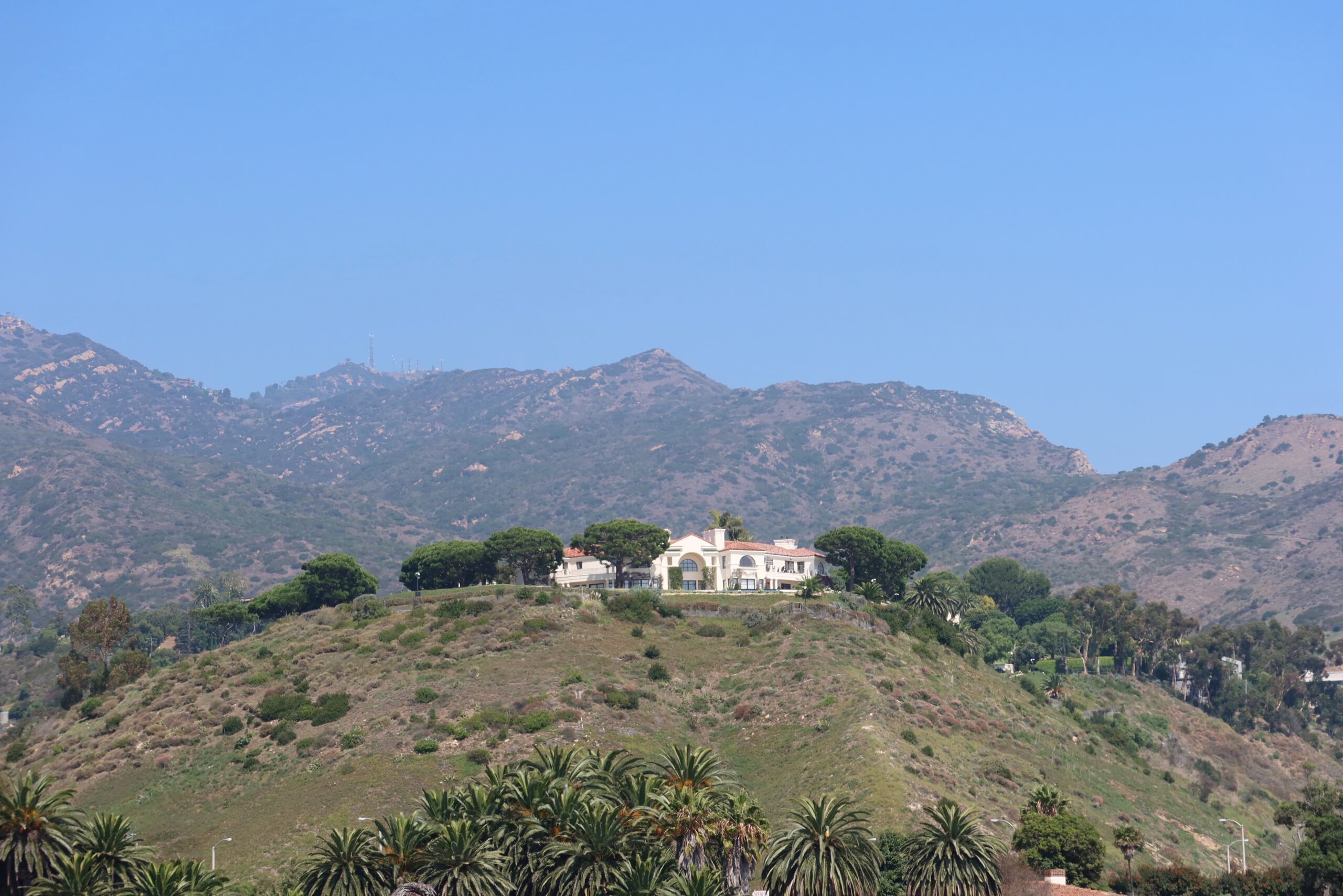 Hillside home overlooking Malibu Lagoon surrounded by palm trees and coastal hills