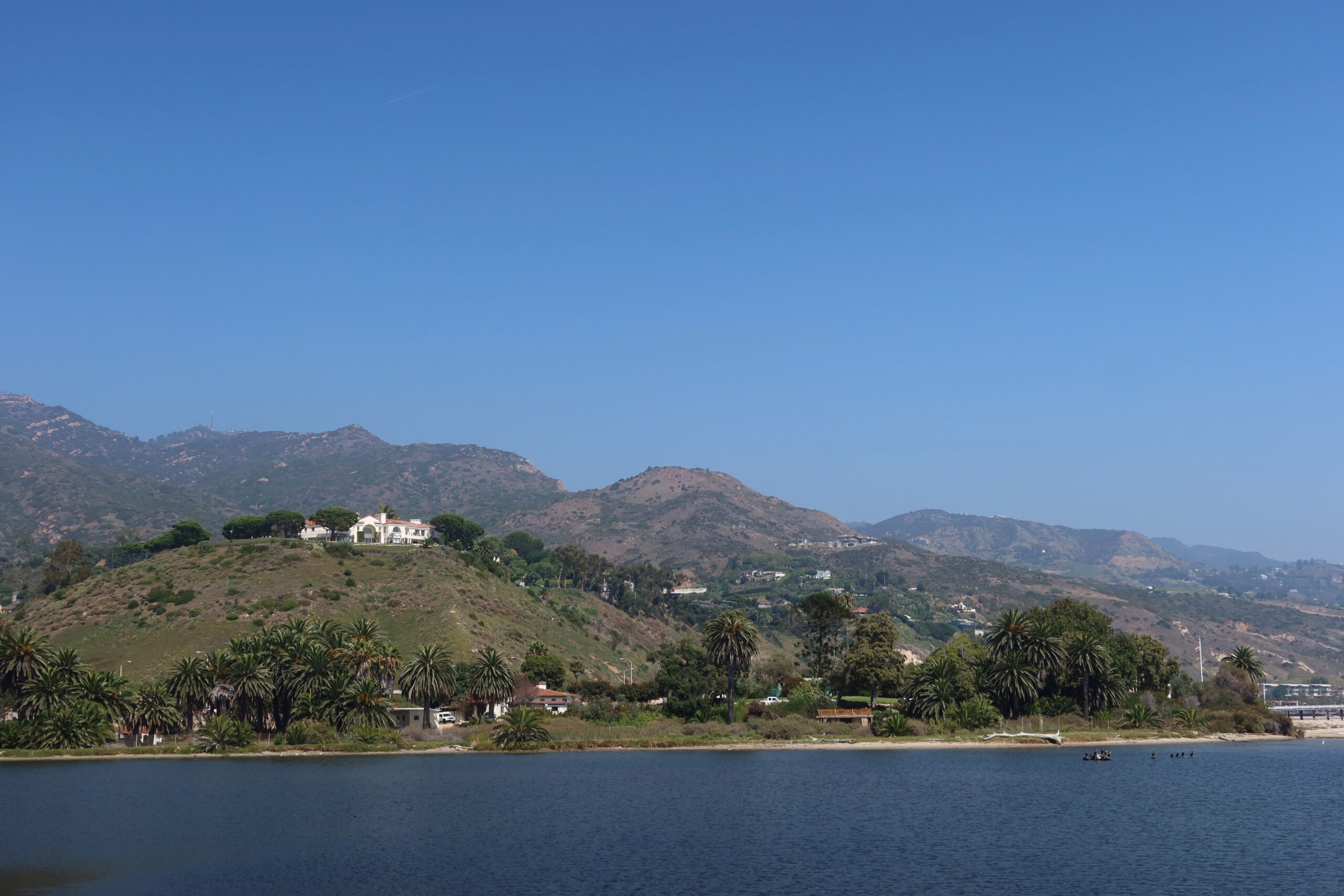 Malibu Lagoon landscape with calm water, palm trees, and rolling hills in the background