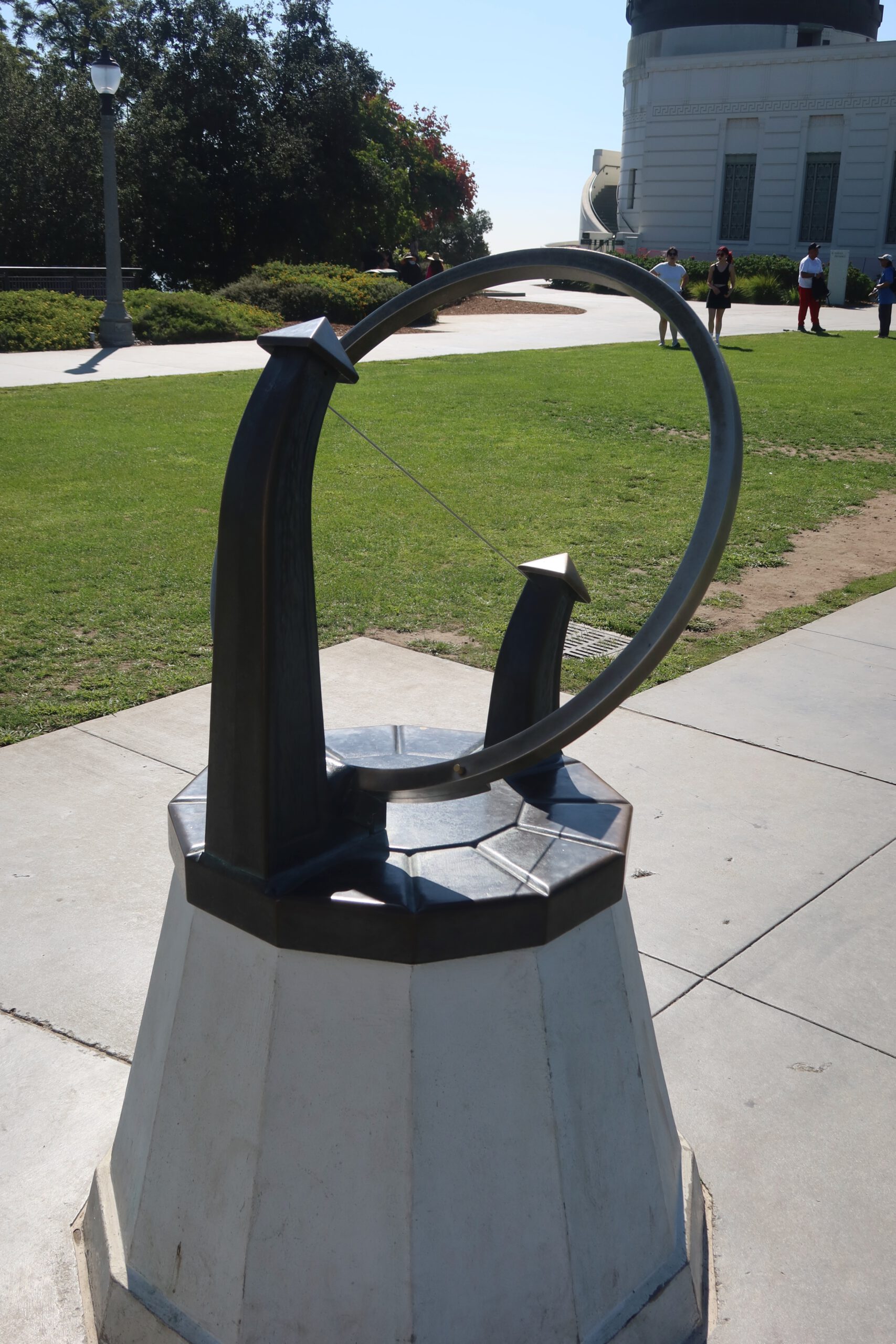 Outdoor astronomical instrument on the lawn at Griffith Observatory, designed to demonstrate celestial alignment, with visitors walking around the observatory grounds in Los Angeles.