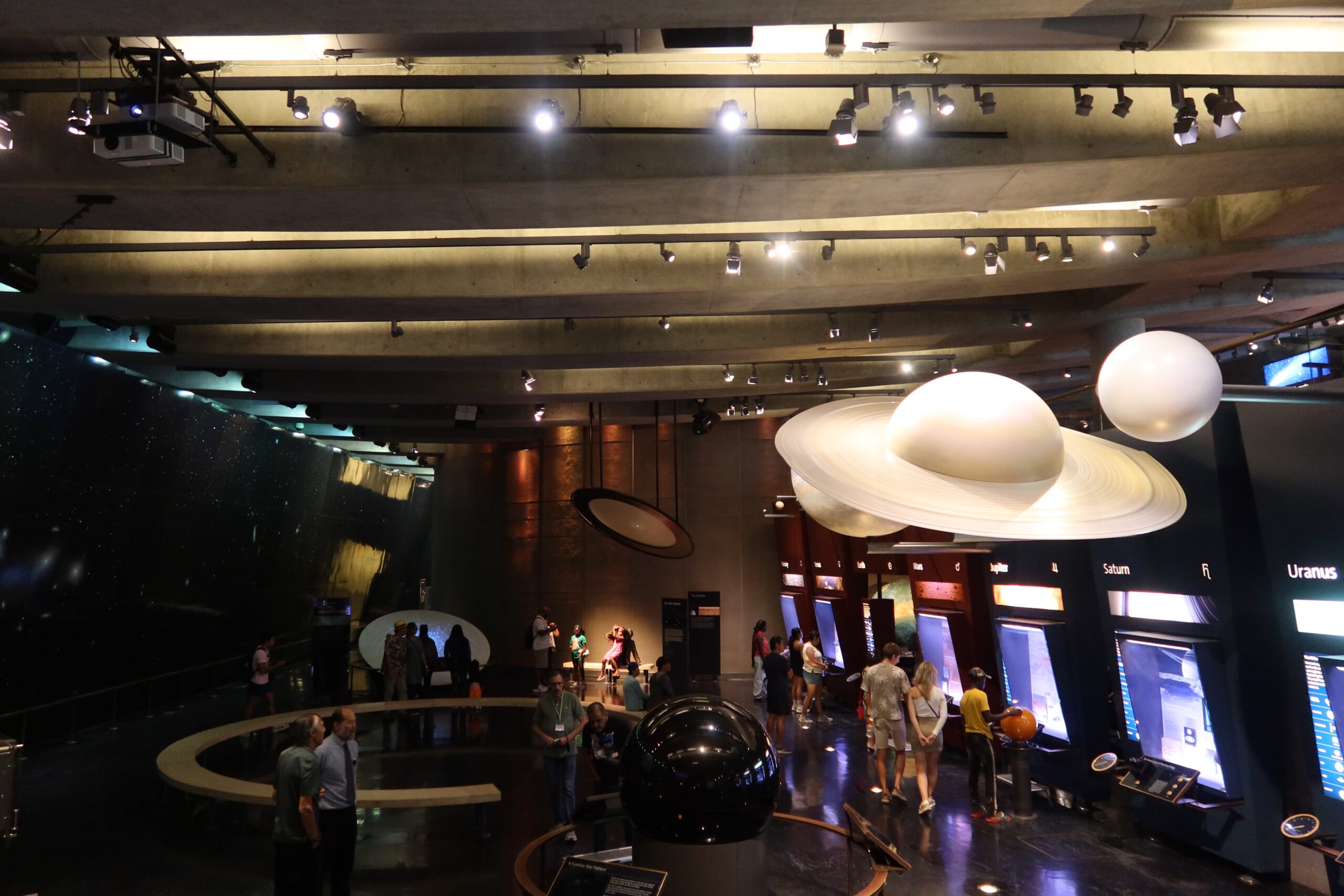 Interior of Griffith Observatory featuring suspended planet models, interactive astronomy exhibits, and visitors exploring the Solar System gallery under dramatic lighting.