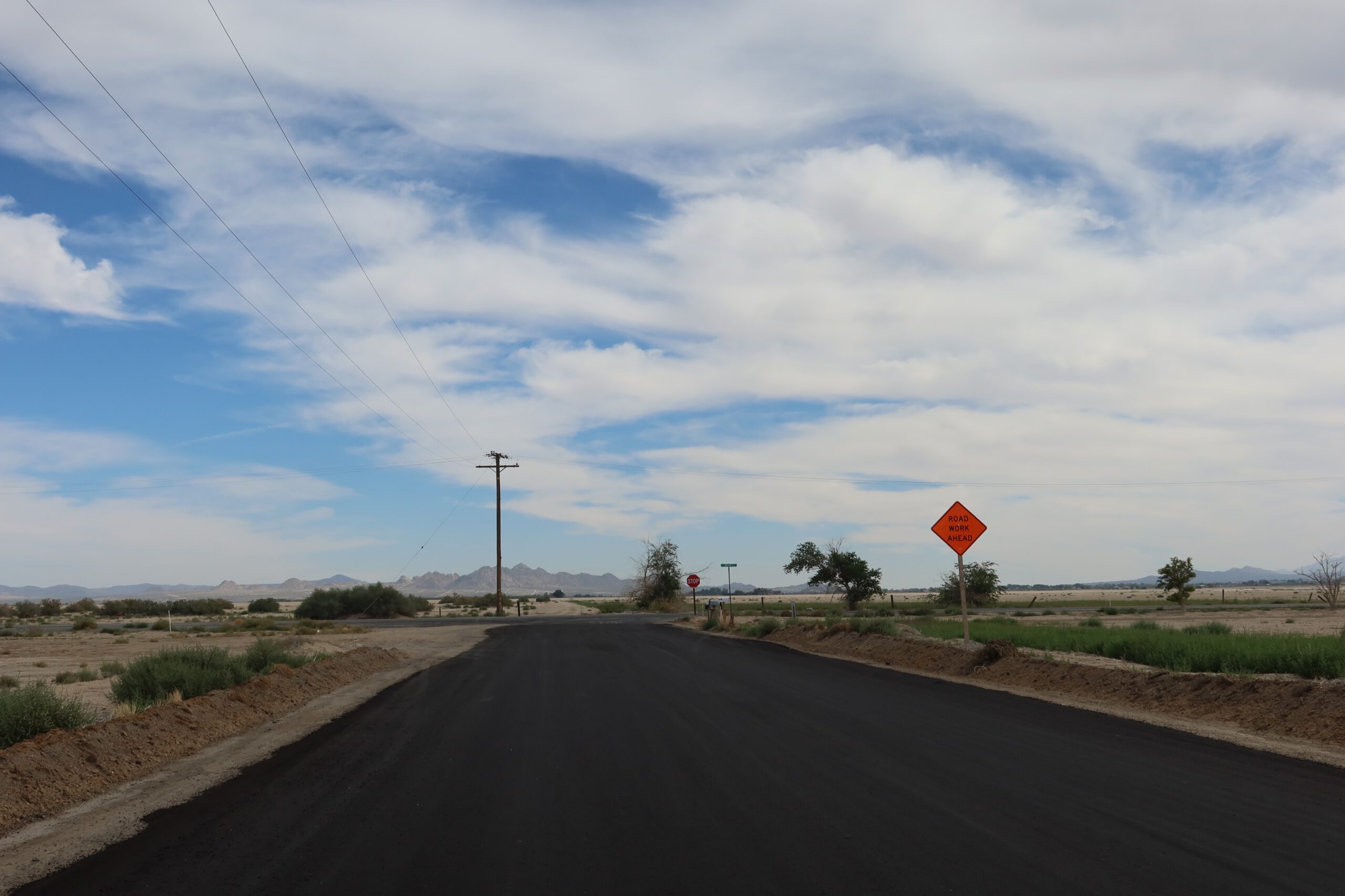 Driving through the Mojave Desert in California on a freshly paved road, with road work signs, open desert surroundings, and expansive skies.