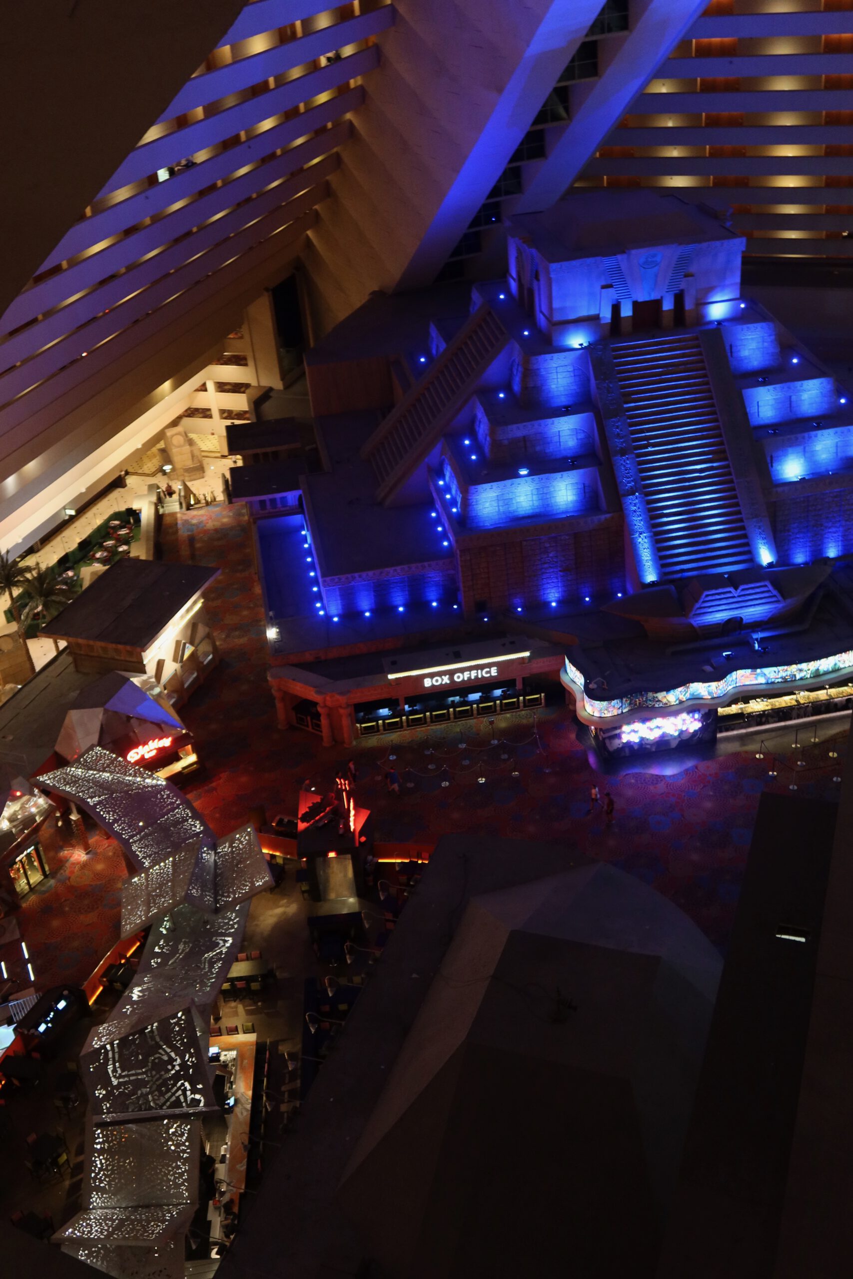 High-angle interior view inside the Luxor Hotel & Casino Las Vegas pyramid, showing the illuminated atrium, box office area, Egyptian-themed architecture, staircases, and walkways lit with blue and ambient lighting at night.