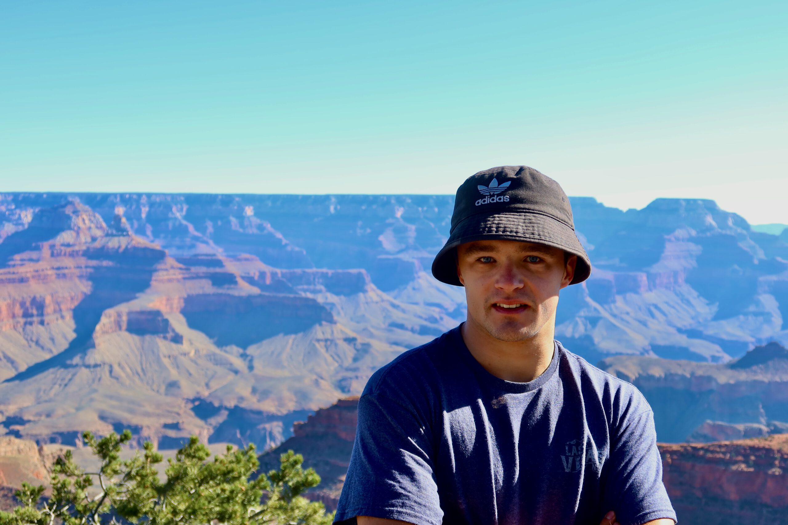 Peter Smit standing at the South Rim of Grand Canyon National Park with layered canyon cliffs and vast desert landscape in the background with an Adidas hat.