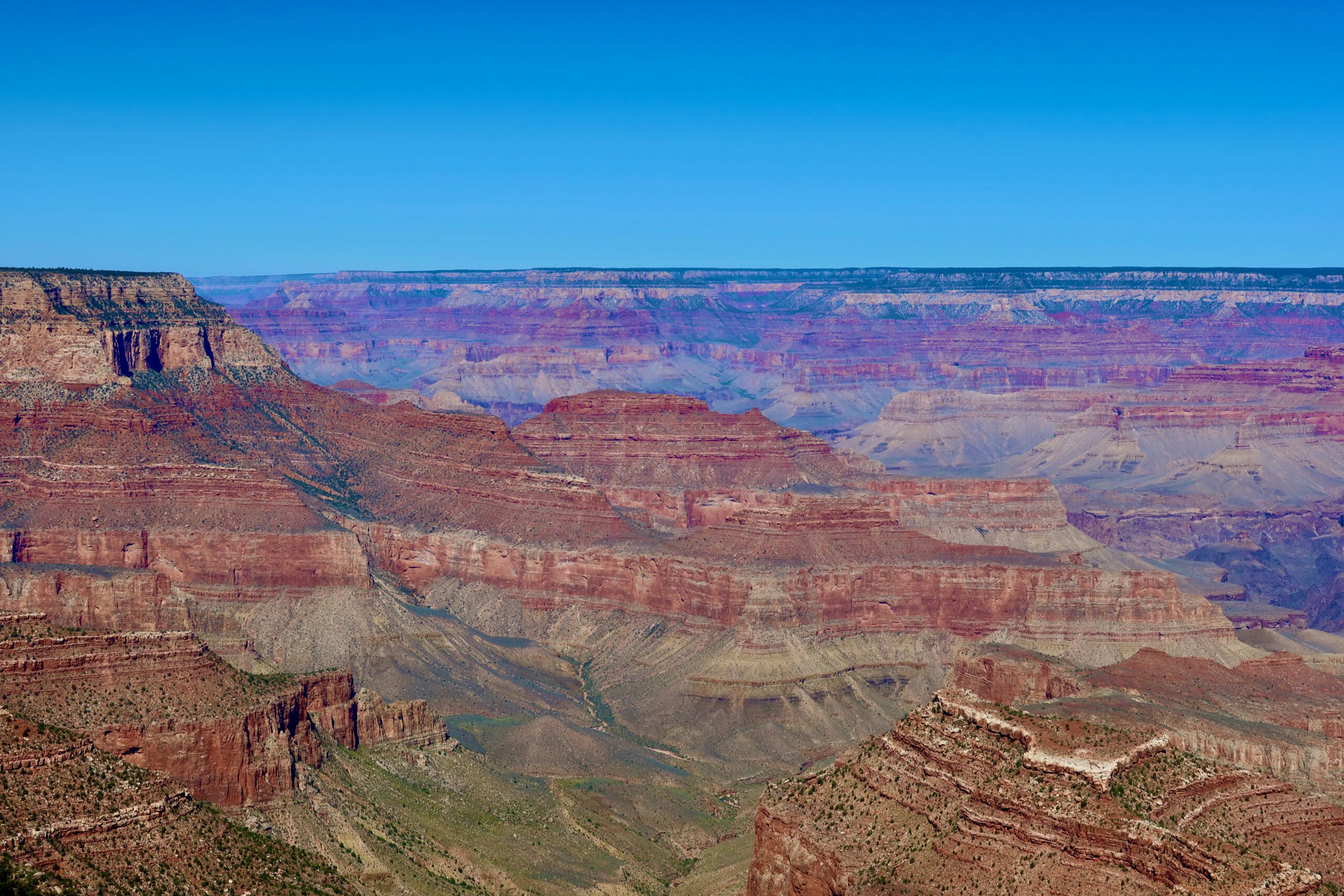 Wide view of layered rock formations inside Grand Canyon National Park showing depth, color contrast, and erosion patterns under a clear sky