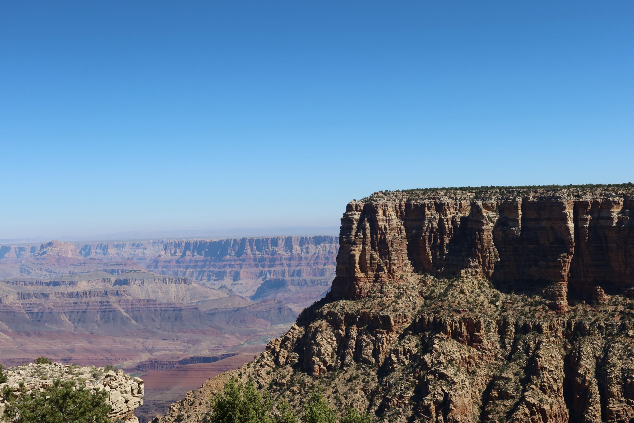 Dramatic cliff formation and layered canyon walls at Grand Canyon National Park with vast desert landscape in the distance