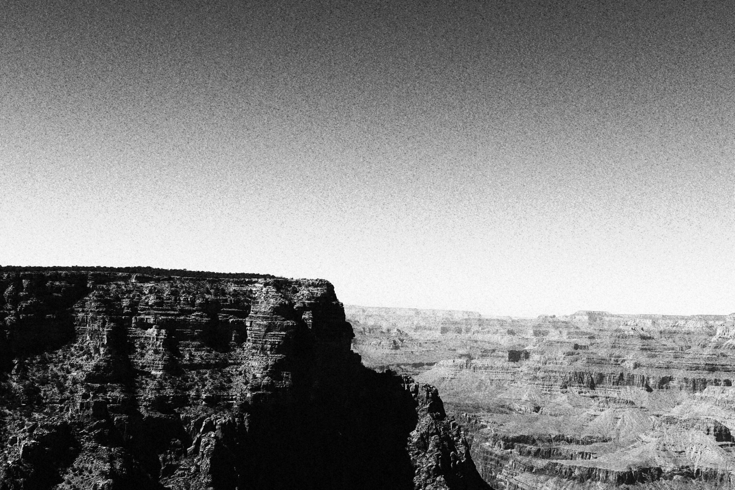 Black and white landscape view of the Grand Canyon showcasing dramatic cliffs, layered rock formations, and vast desert depth