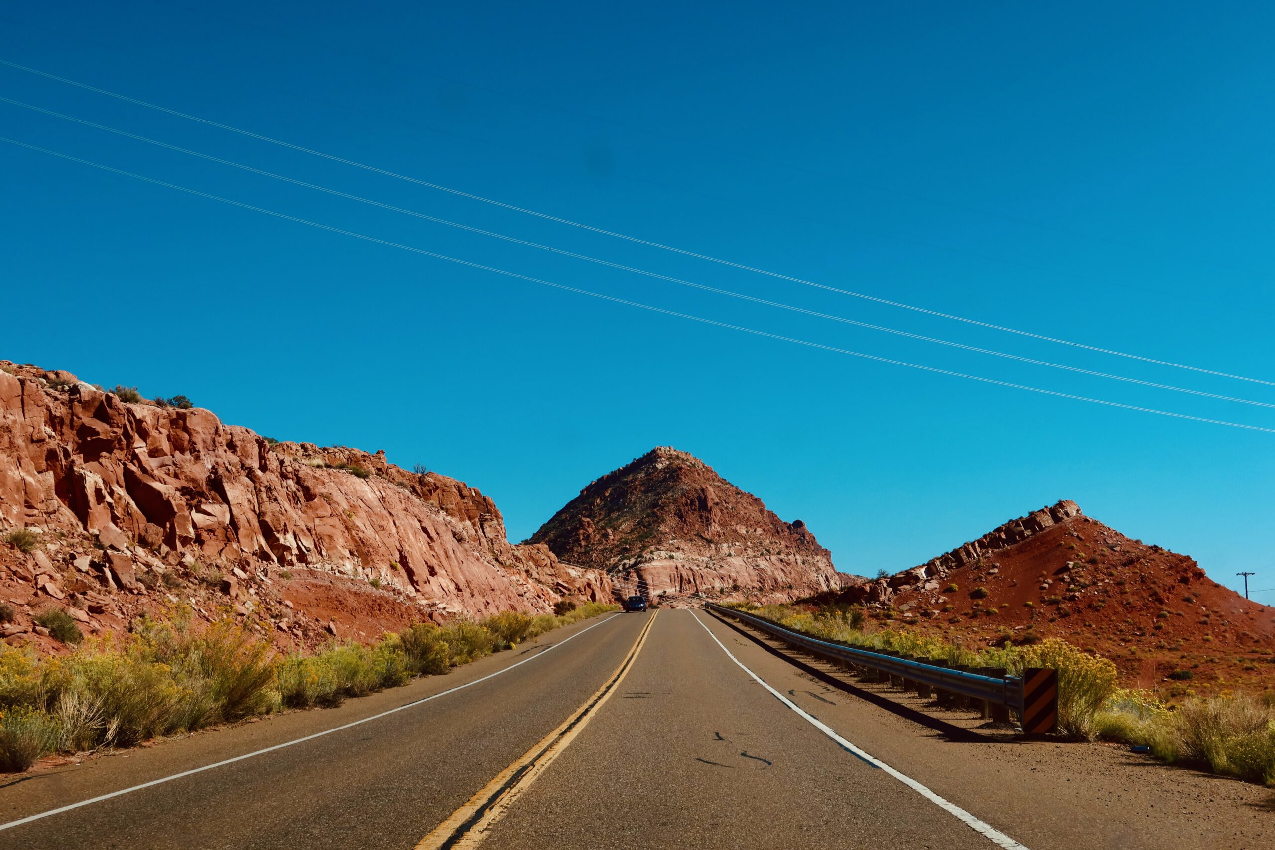 Desert highway near Glen Canyon with red rock cliffs and open road leading toward Utah, classic Southwest road trip scenery under a clear blue sky near Page, Arizona