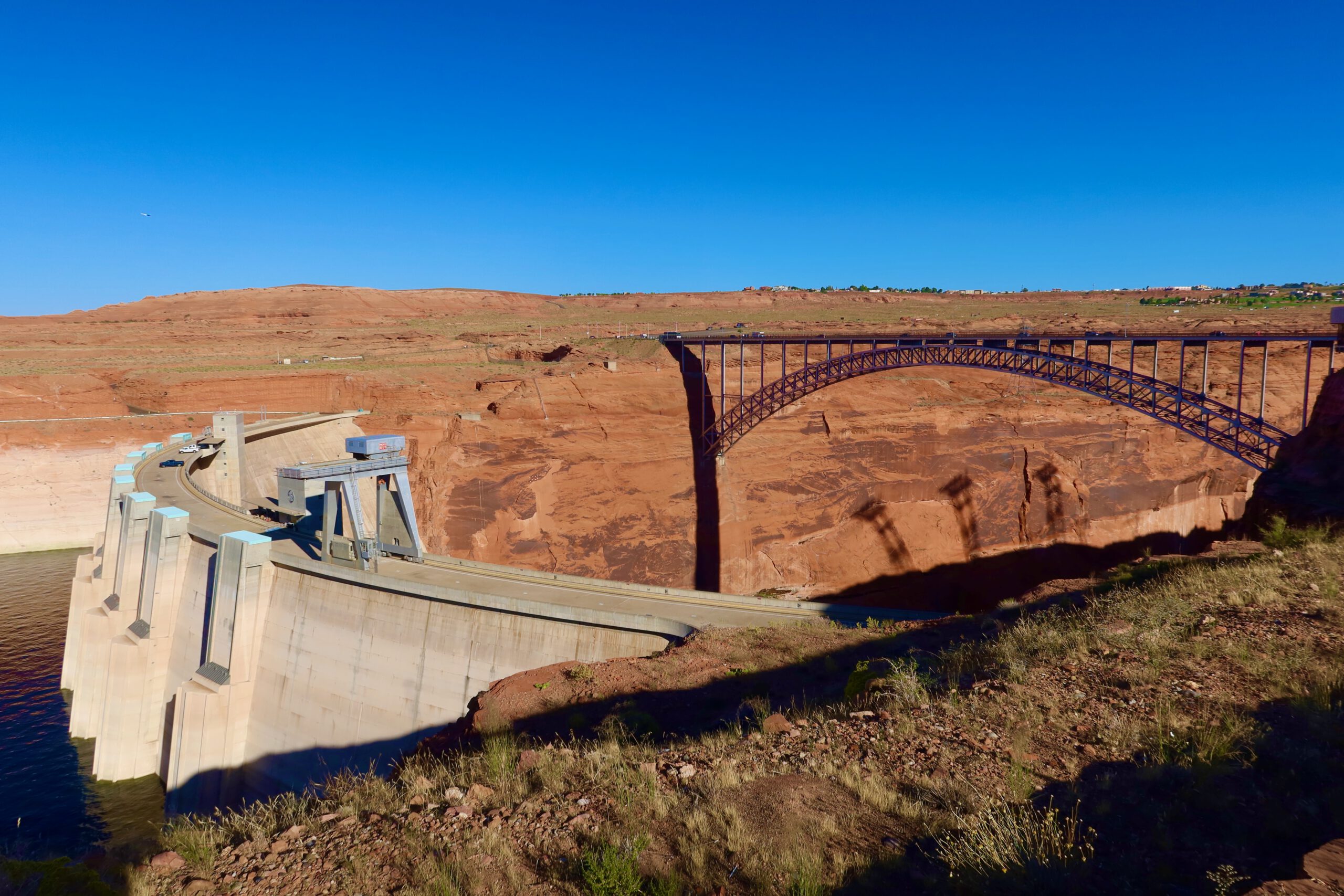 Glen Canyon Dam and Glen Canyon Dam Bridge overlooking Lake Powell near Page, Arizona, with dramatic red rock canyon walls and clear blue desert sky.