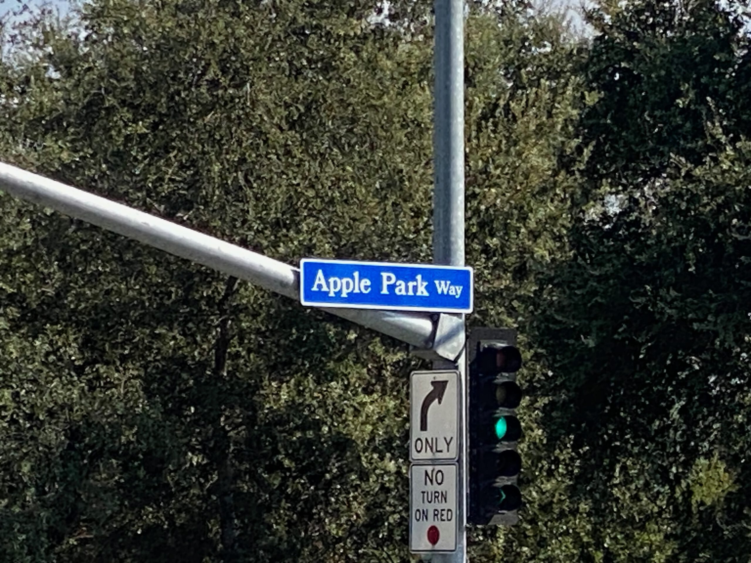 Apple Park Way street sign at an intersection in Cupertino, marking the road leading to Apple Park headquarters, with traffic lights and trees in the background.