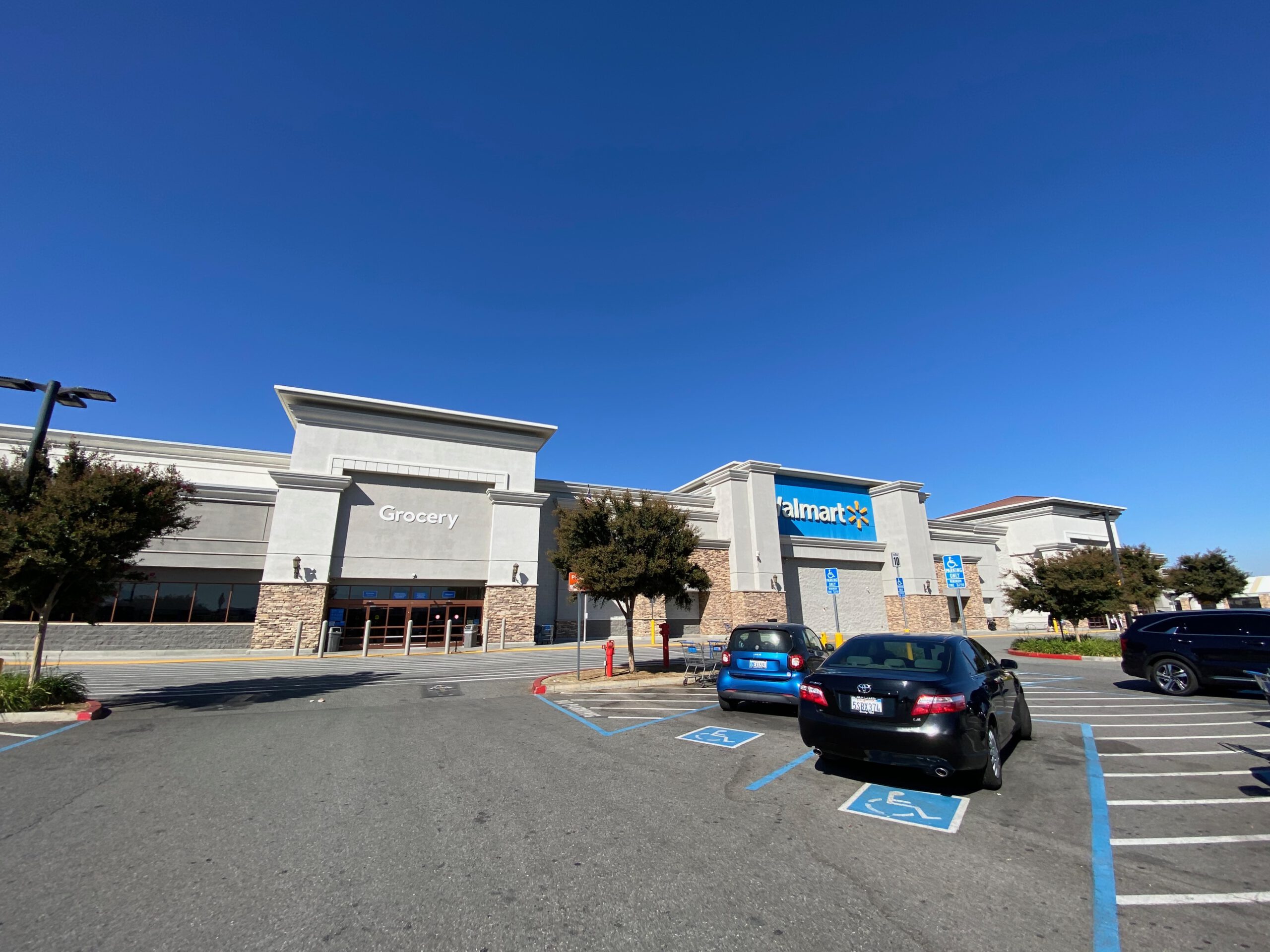 Wide exterior view of Walmart Supercenter Beaumont California showing the grocery entrance, large Walmart logo, spacious parking lot with handicap parking spaces, cars in front of the store, and a clear blue California sky.