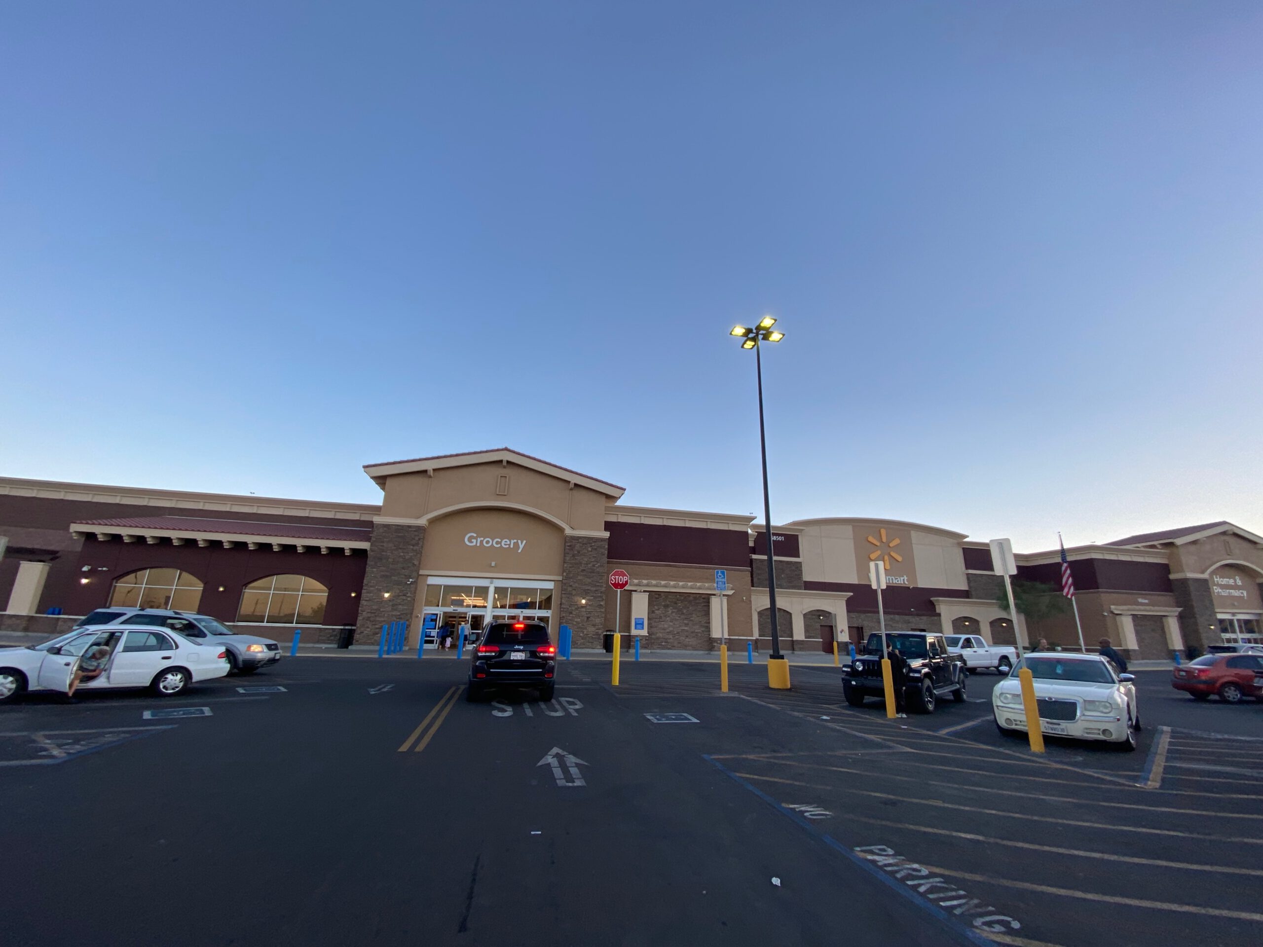 Walmart Yucca Valley Supercenter photographed in the evening, with cars parked in front and the grocery entrance lit against a clear desert sky.