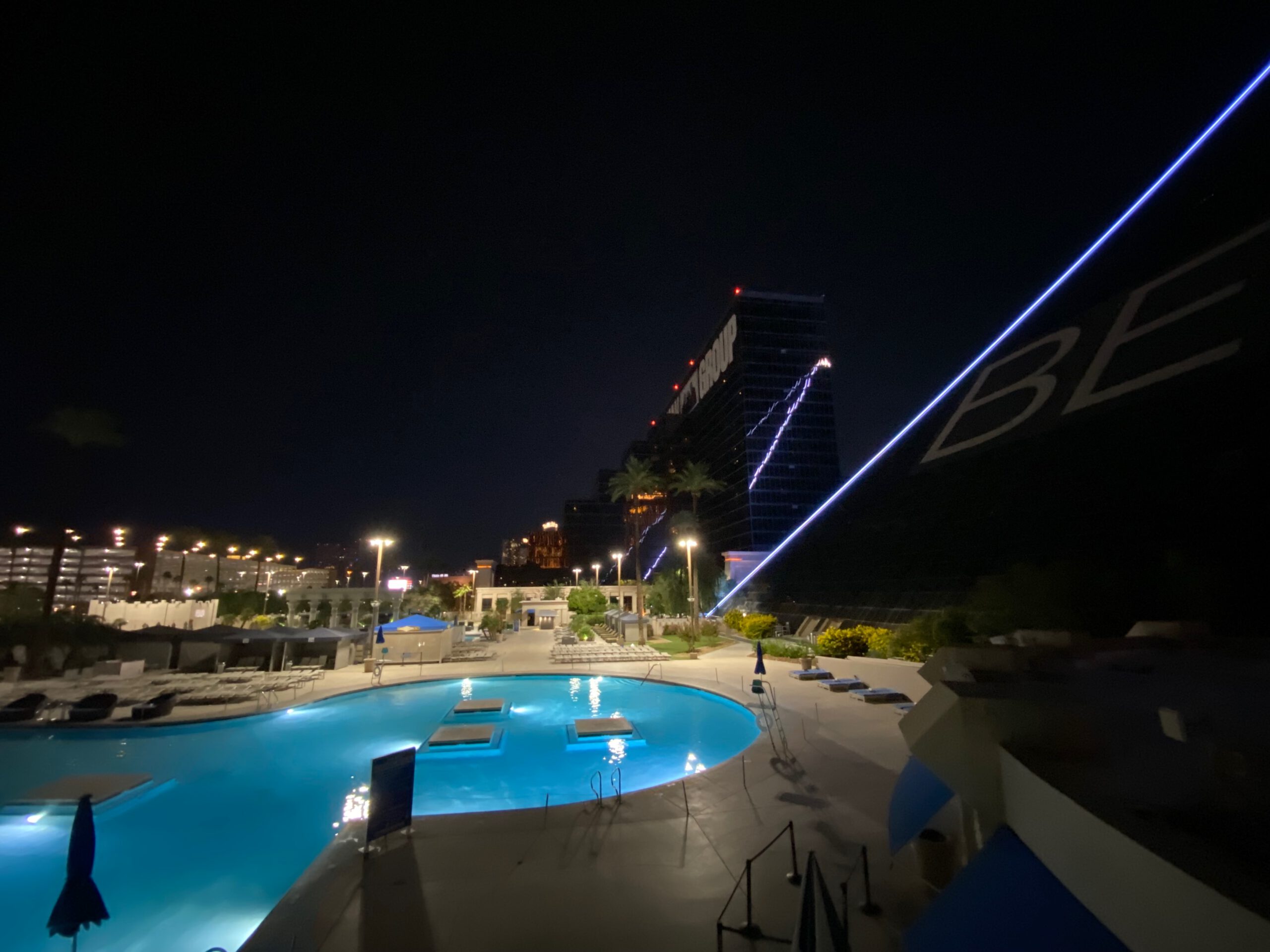 Nighttime view of the Luxor Resort pool area on the Las Vegas Strip, with illuminated swimming pool, palm trees, and the glowing pyramid facade visible in the background.