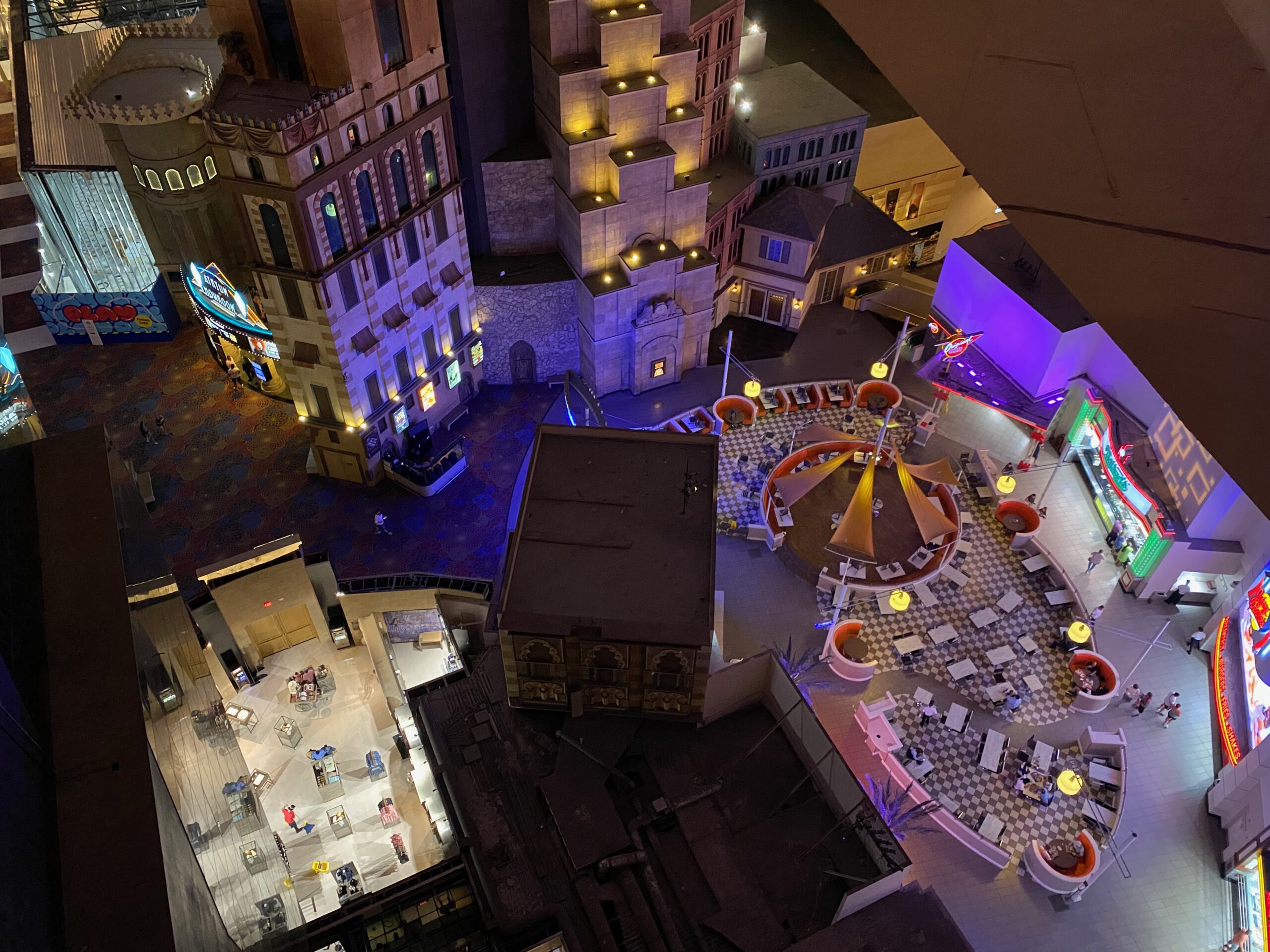 Overhead night view inside the Luxor Hotel & Casino Las Vegas, showing the interior atrium with themed architectural facades, illuminated walkways, restaurants, seating areas, and colorful lighting viewed from high inside the pyramid.