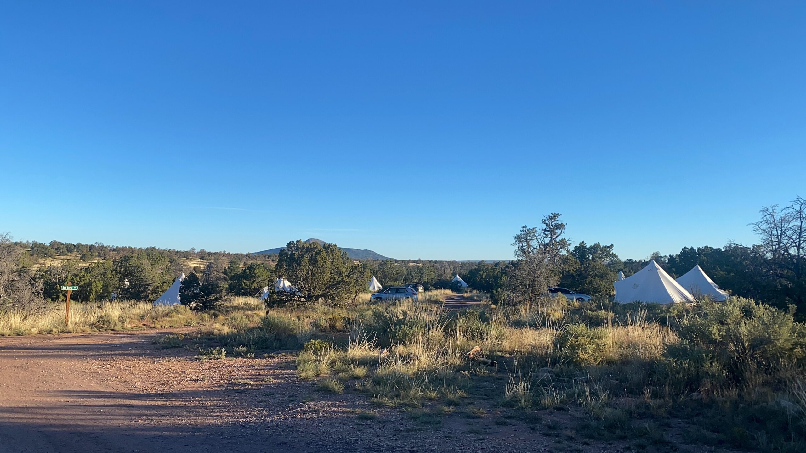 Wide view of Wander Camp Grand Canyon with multiple glamping tents spread across the Arizona high desert, surrounded by nature under a clear blue sky