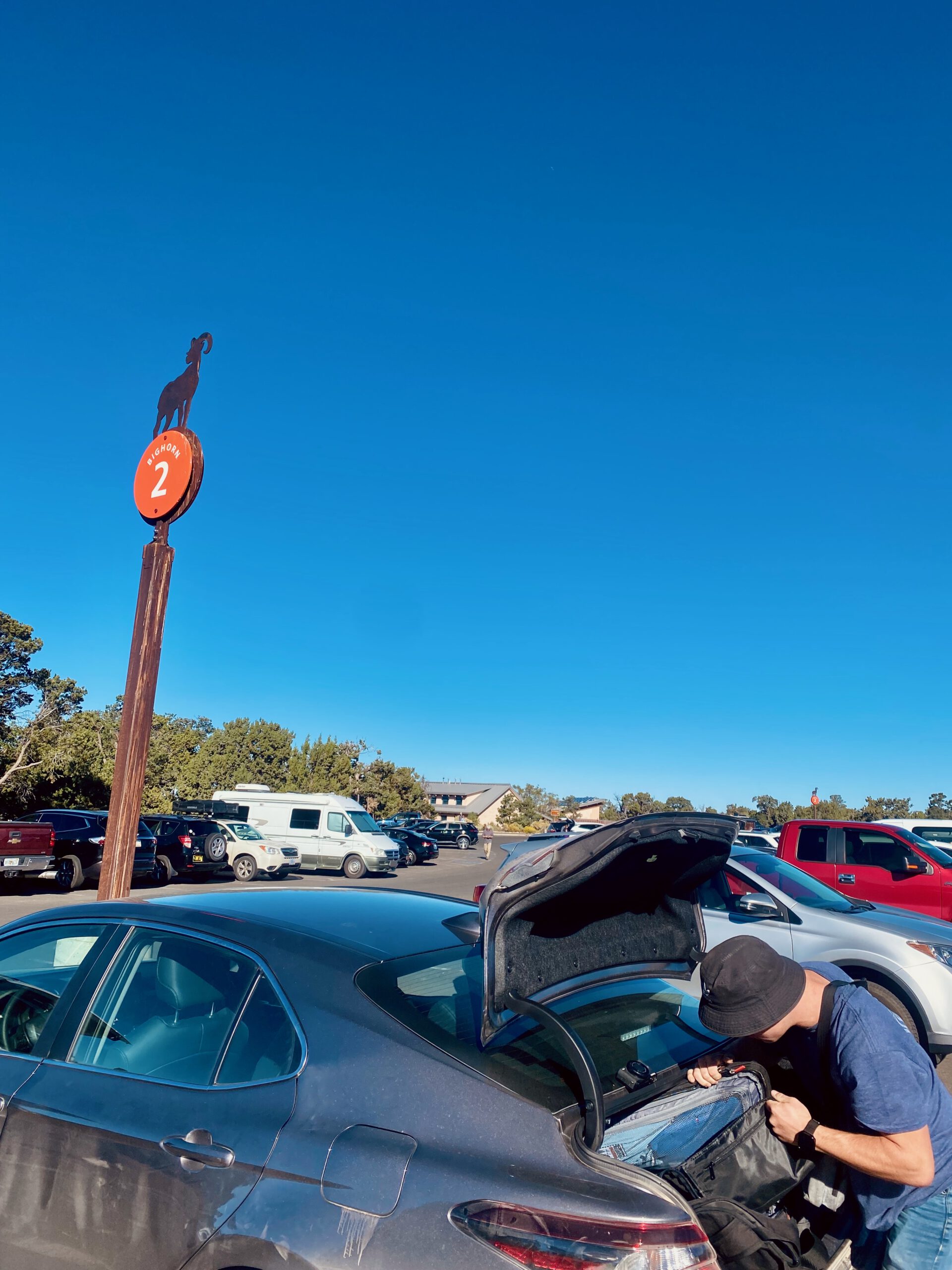 Traveler unpacking luggage at a parking area near the South Rim of Grand Canyon National Park under a clear blue Arizona sky