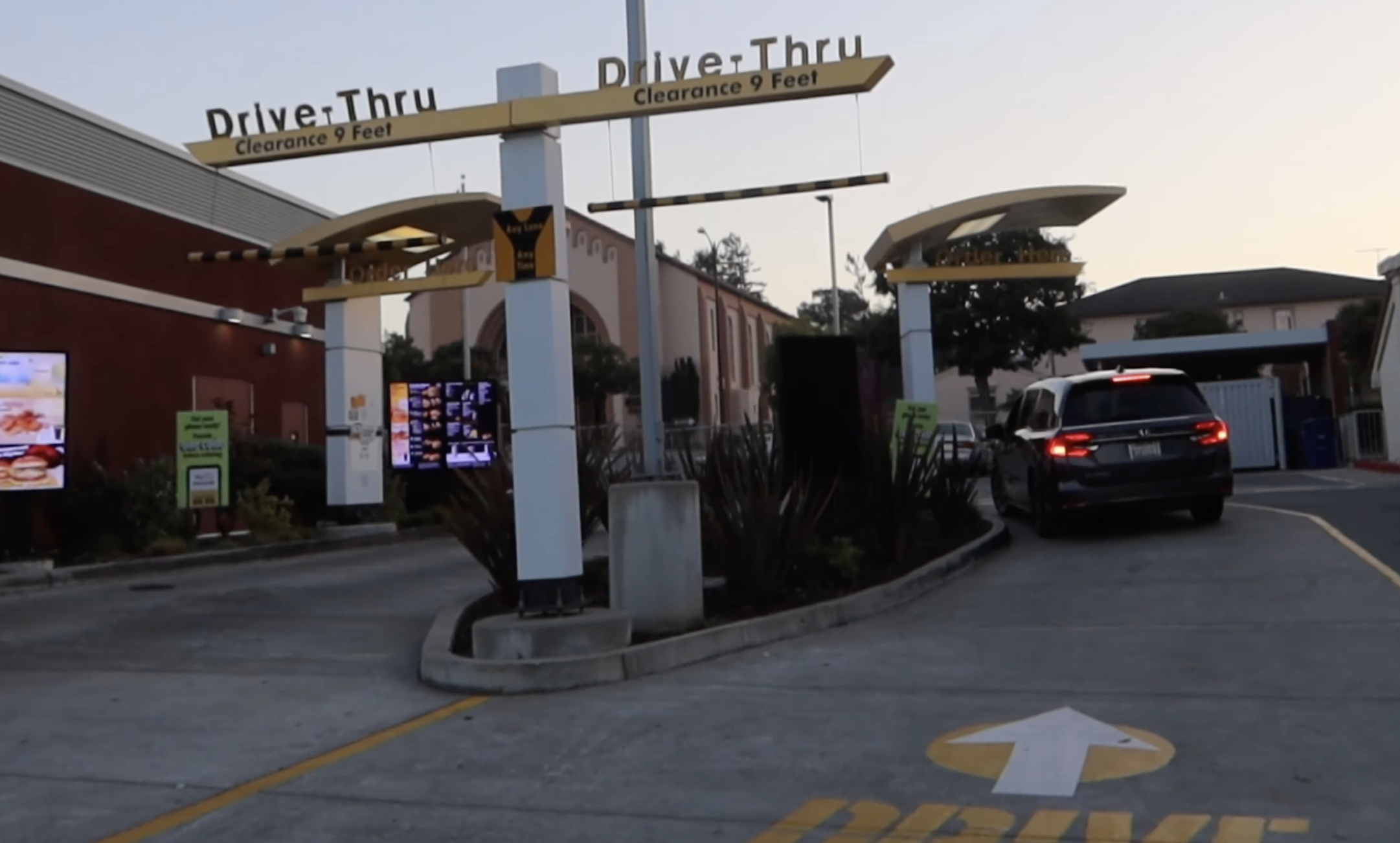 Evening view of the drive-thru at McDonalds Millbrae El Camino Real with illuminated menu screens and vehicles in line near SFO