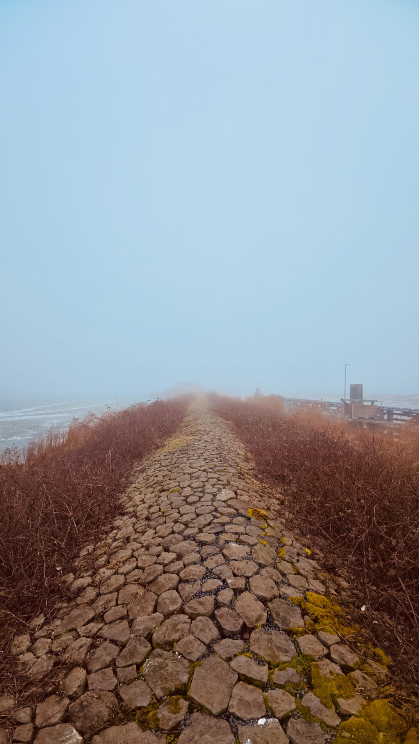 Walking Kornwerderzand on a stone walking path near the Afsluitdijk, misty view with water, wind and industrial sluice structures