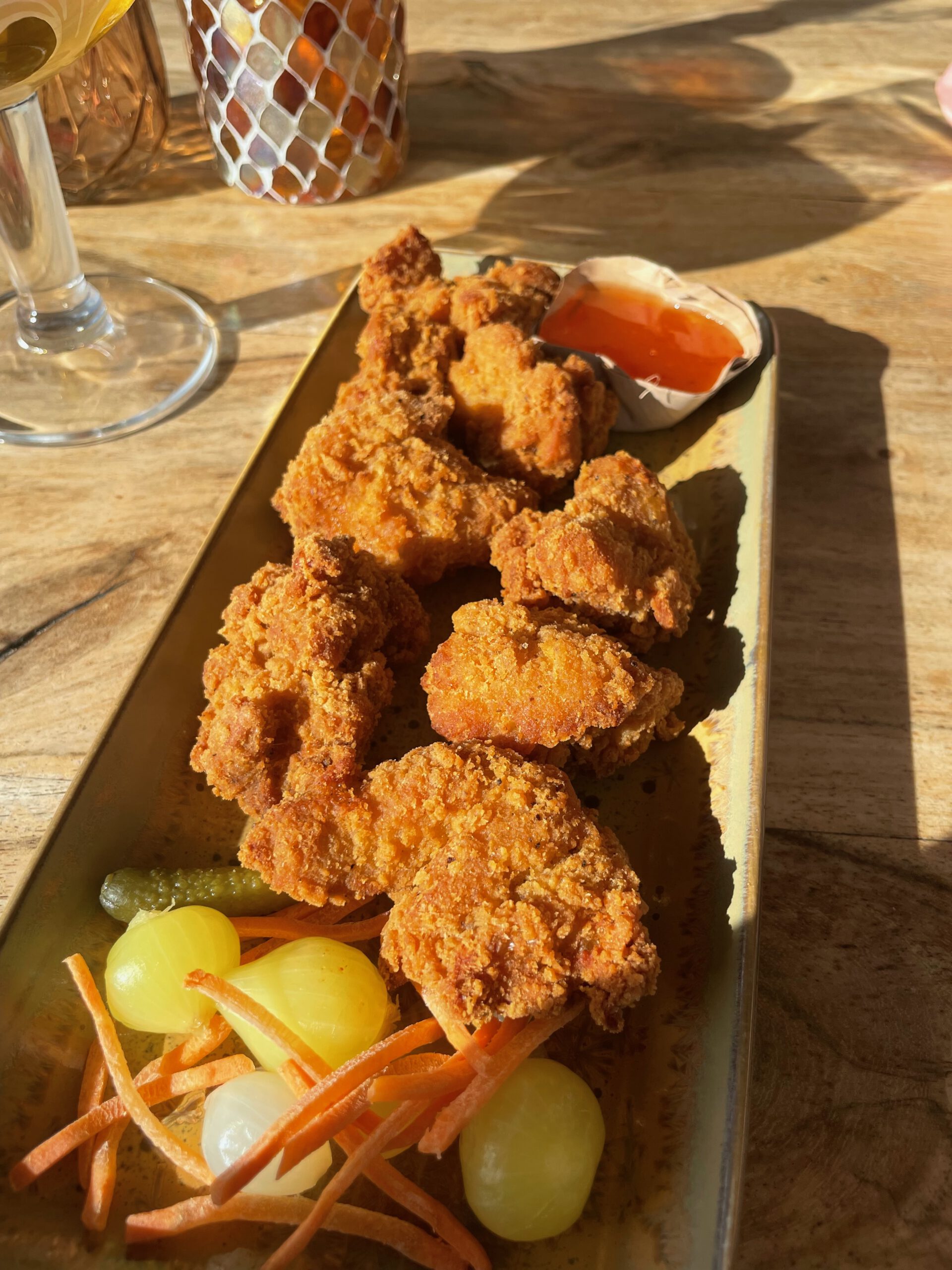 Golden crispy fried chicken bites with pickled vegetables and sweet chili sauce at Strandrestaurant Nederzandt Noordwijk, served as a warm beach snack in natural sunlight