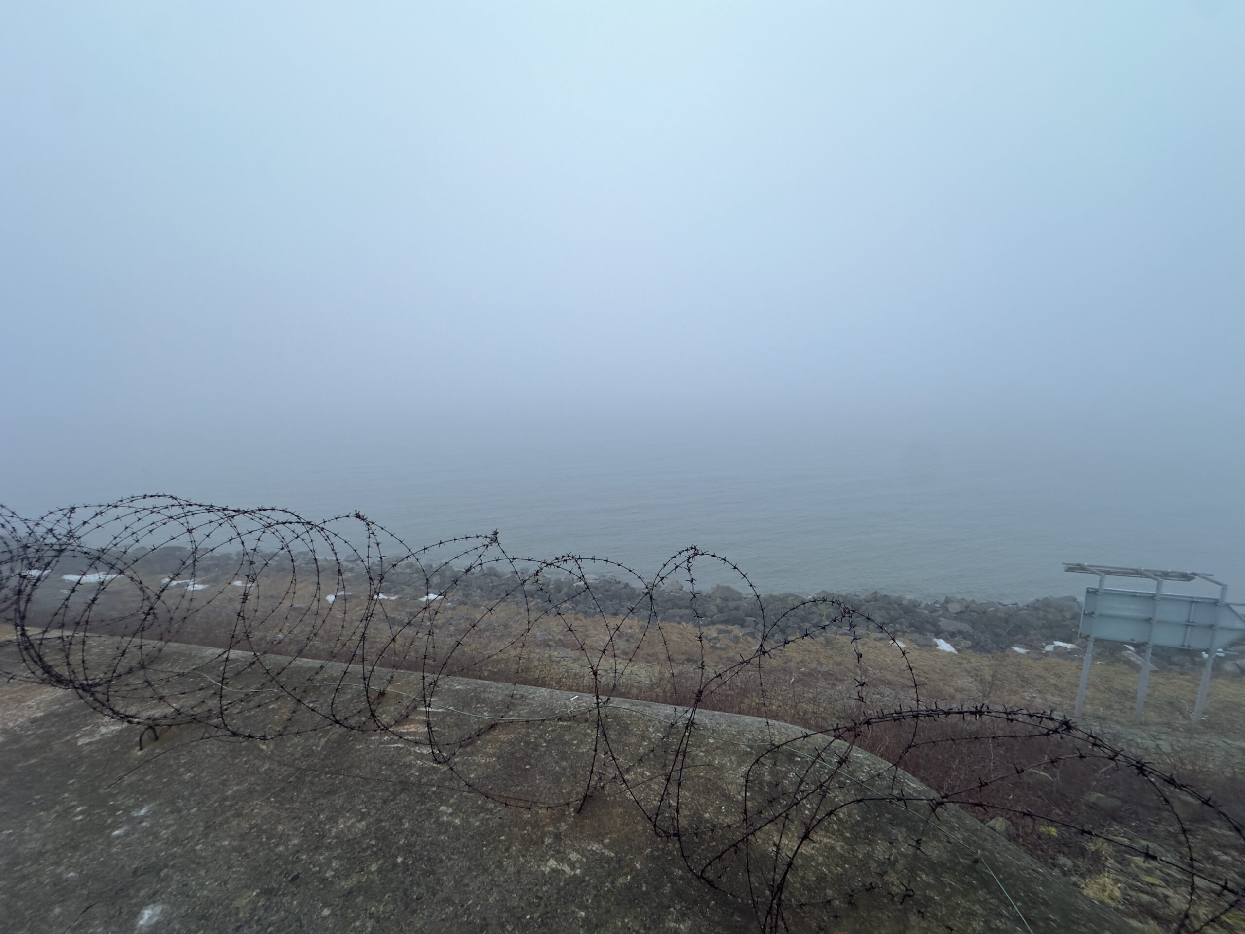 Walking Kornwerderzand along a foggy stone path on the Afsluitdijk, surrounded by rough vegetation and silence