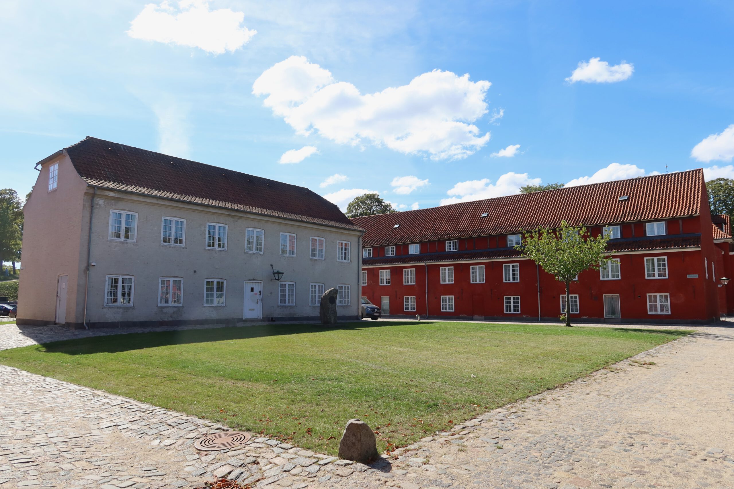 Kastellet Copenhagen inner courtyard with historic military buildings, green lawn and red barracks under a blue sky