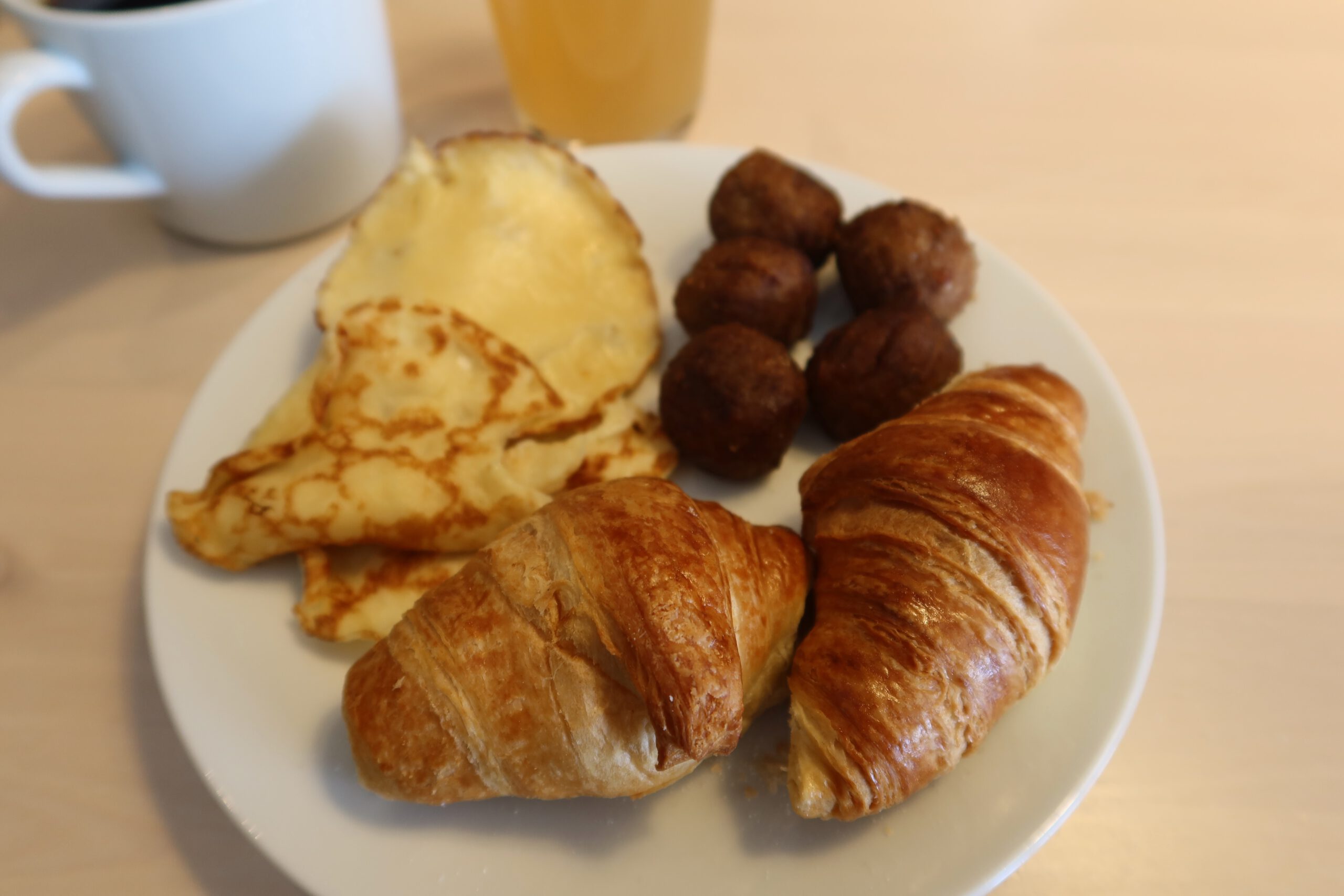 Breakfast plate at IKEA Hotell Älmhult with croissants, Swedish meatballs and thin pancakes, served alongside coffee and juice during the morning buffet.