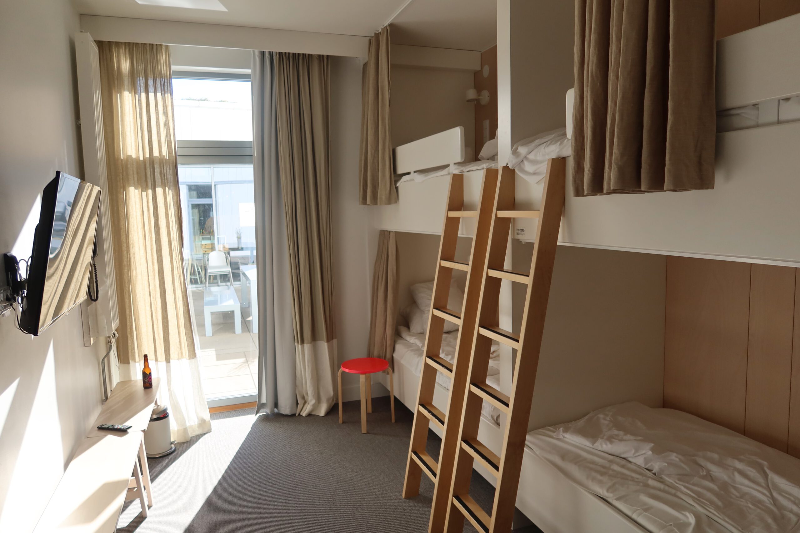 Family room at IKEA Hotell Älmhult featuring two wooden bunk beds with ladders, clean white bedding, soft curtains, natural daylight and a compact Scandinavian hotel room layout.