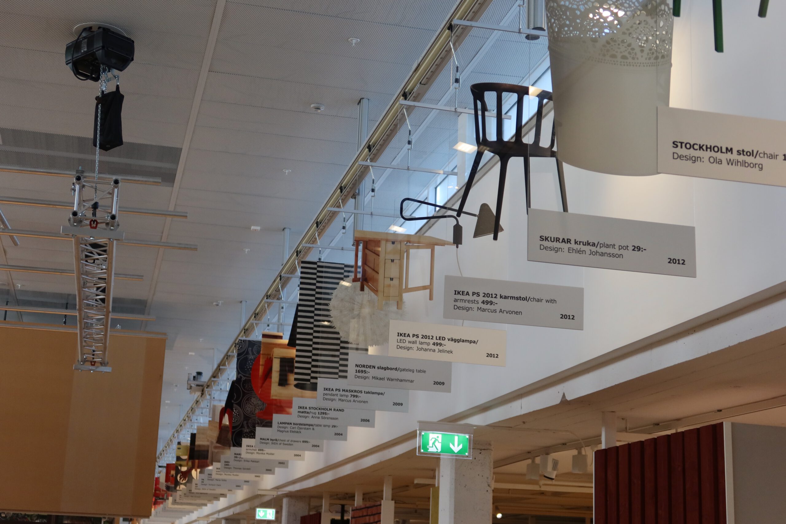 IKEA Museum Älmhult interior exhibition showing suspended iconic IKEA furniture designs with product labels and design history timeline