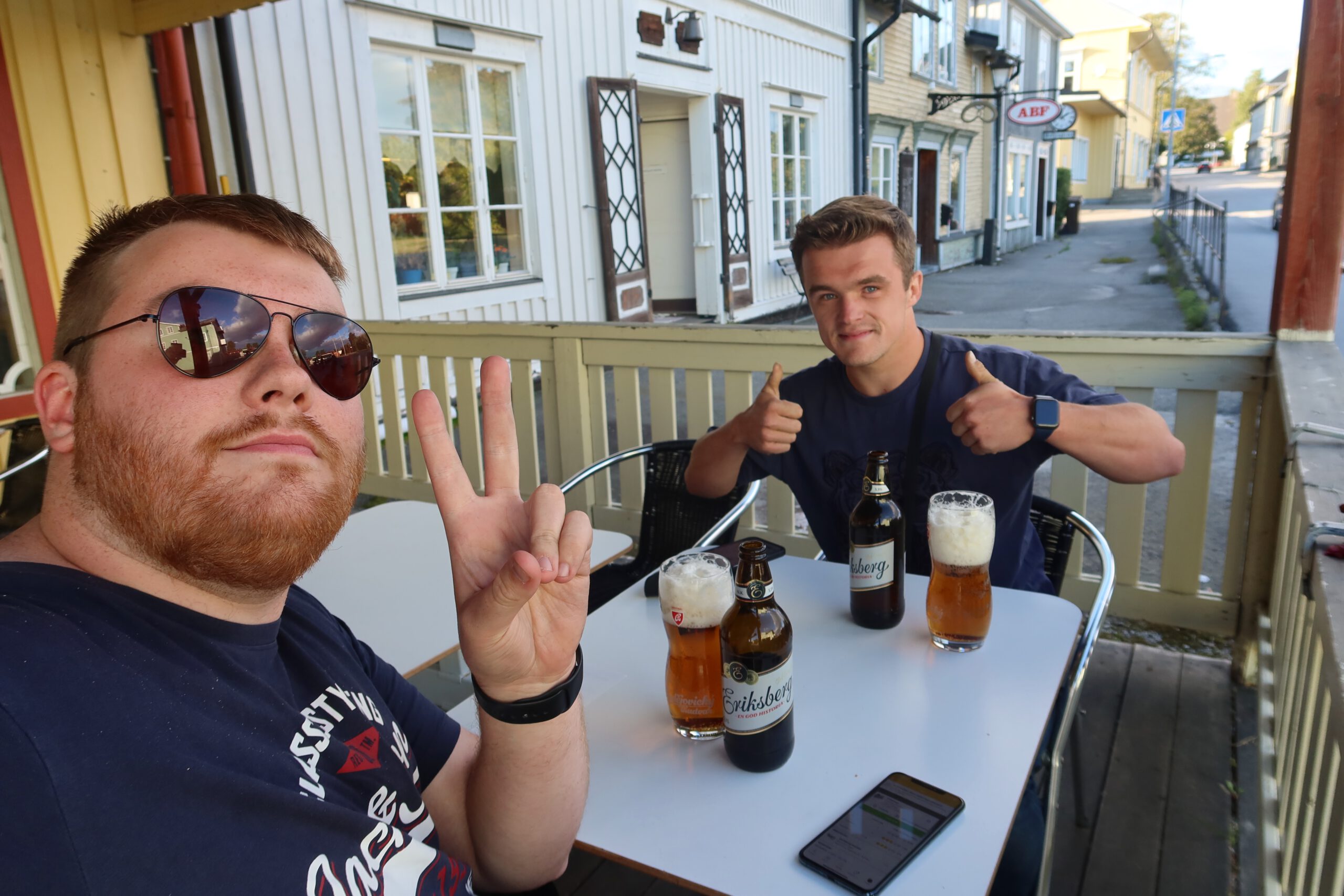 Timo van den Berg and Peter smit at Sun Rise Nordmaling social moment on the outdoor terrace with two travelers enjoying Swedish beer together, relaxed vibes and friendly small town atmosphere during a road trip through northern Sweden