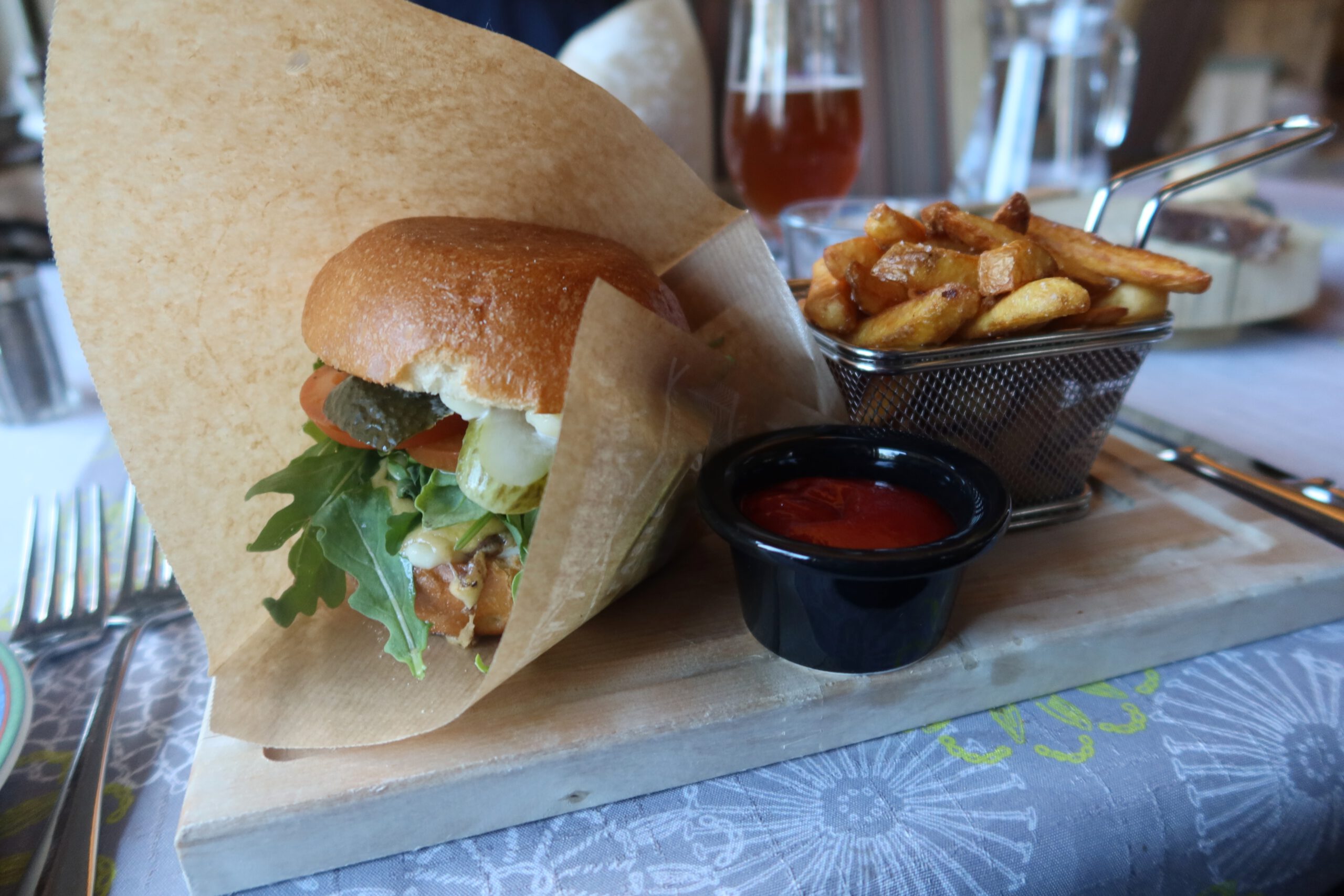 Lapland Hotels Hetta restaurant reindeer burger served on a wooden board with brioche bun, lettuce, pickles, tomato, fries in a metal basket and ketchup in Enontekiö