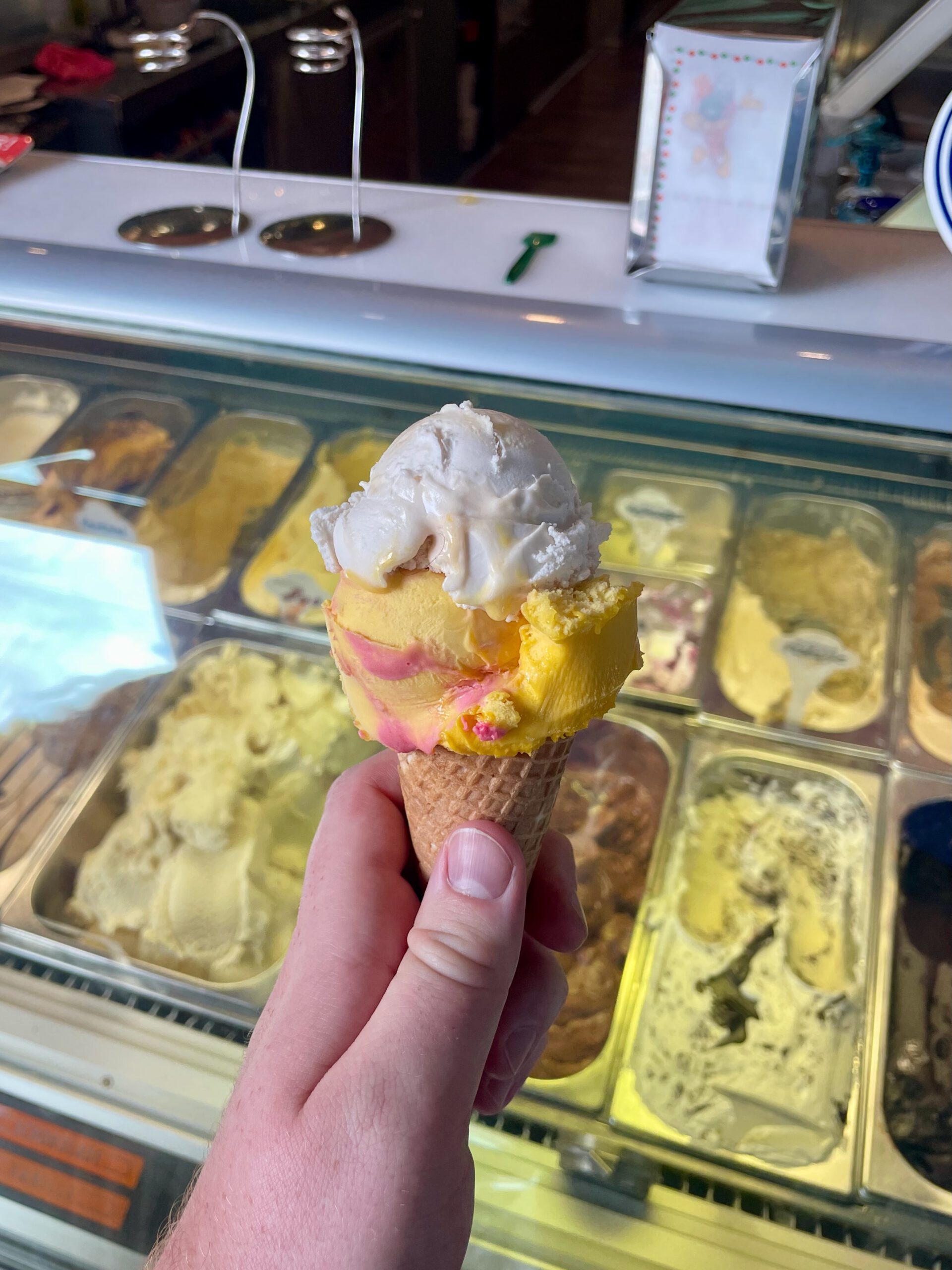 Ice cream cone at Eiscafé La Vita Wuppertal with German scoop ice cream held in front of the ice cream display