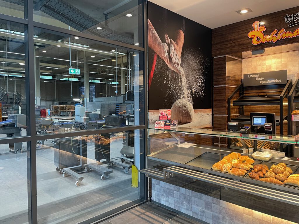 Bakery Dahlmann Wuppertal interior, open production kitchen visible behind glass with fresh bread display and modern bakery cafe seating area