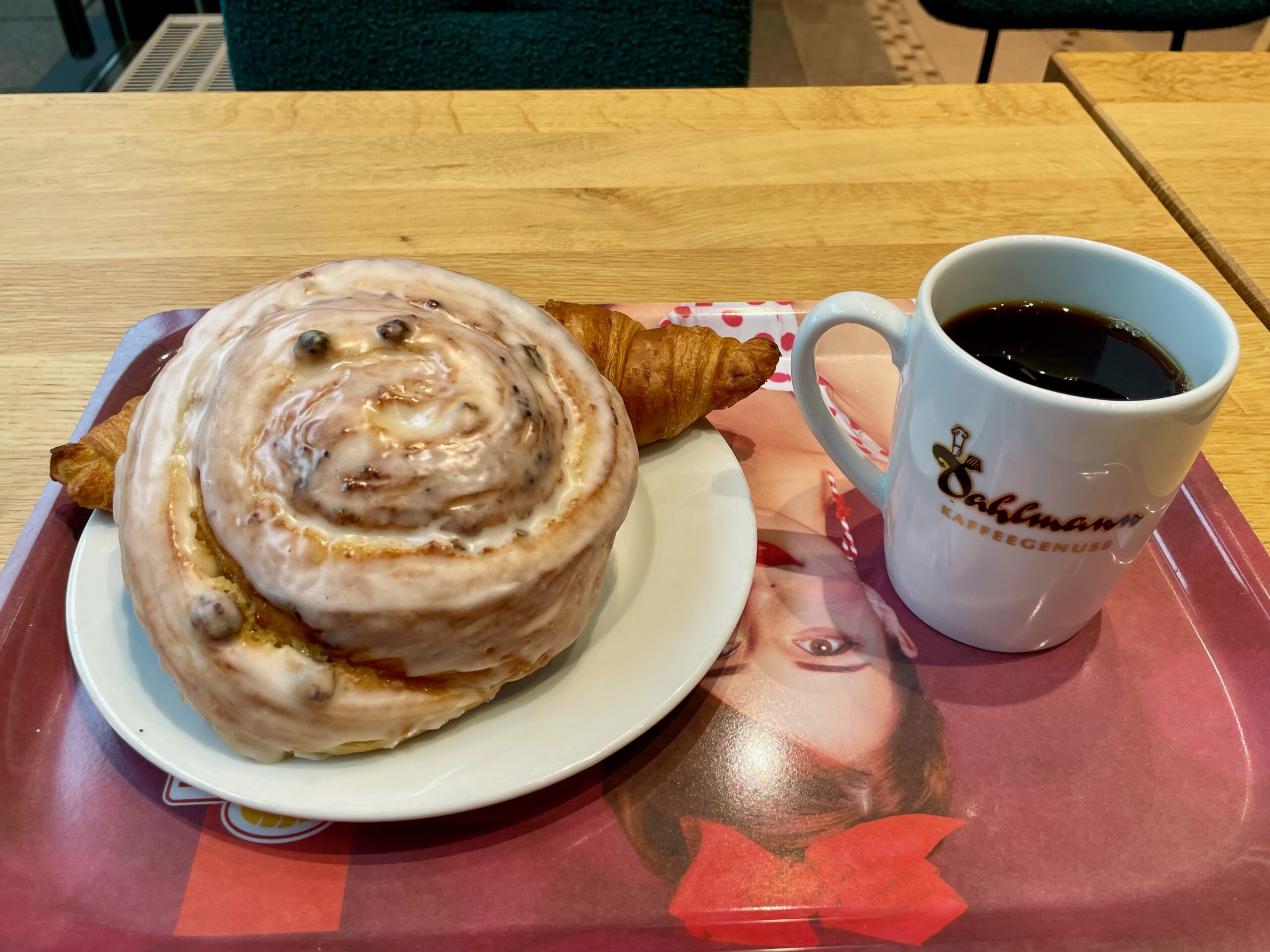 Bakery Dahlmann Wuppertal breakfast, cinnamon roll with icing, fresh croissant and black coffee served on a table inside the bakery cafe