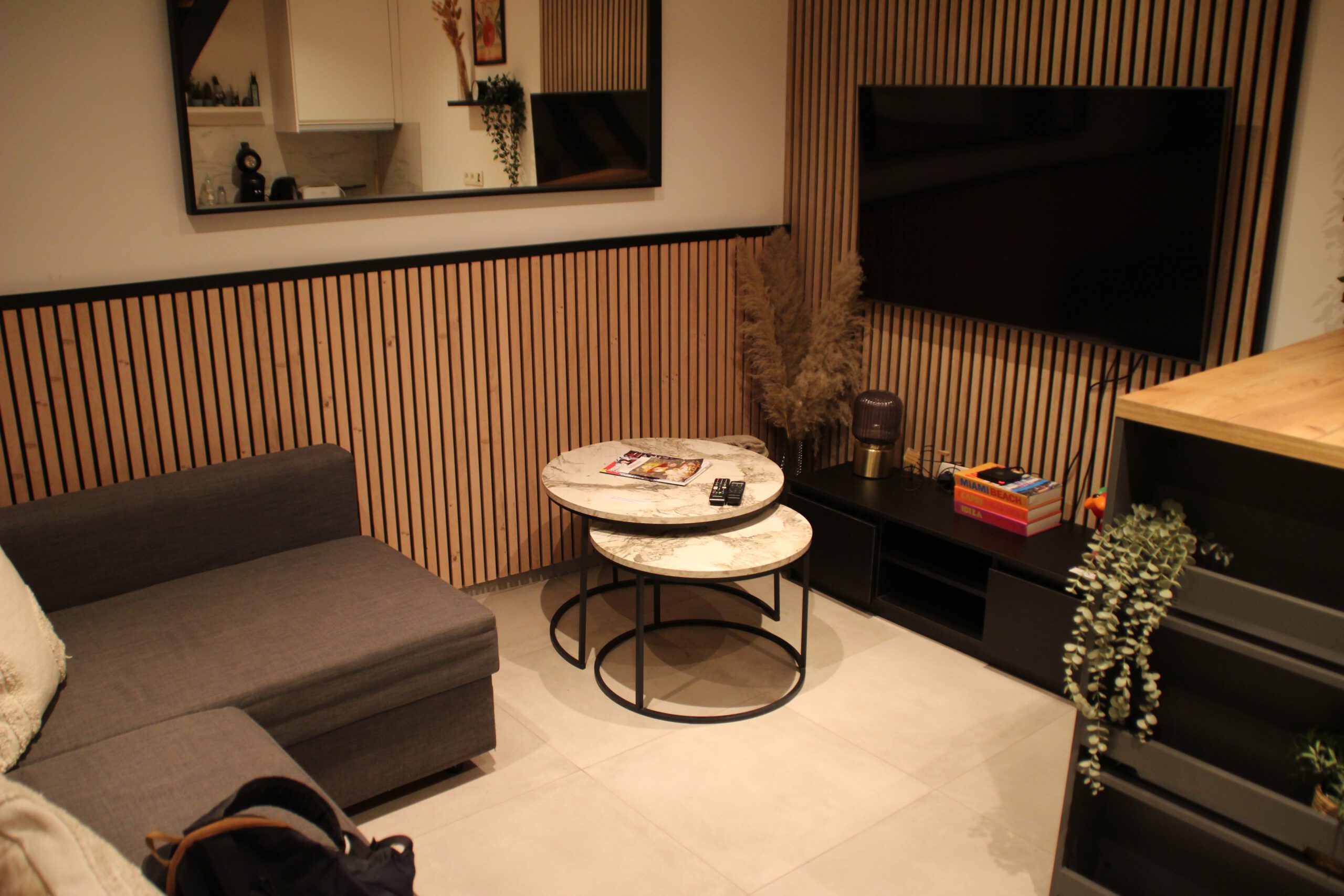 Le cocon de Chênée Liège living room interior, modern seating area with wall-mounted TV, wooden paneling, and compact lounge setup