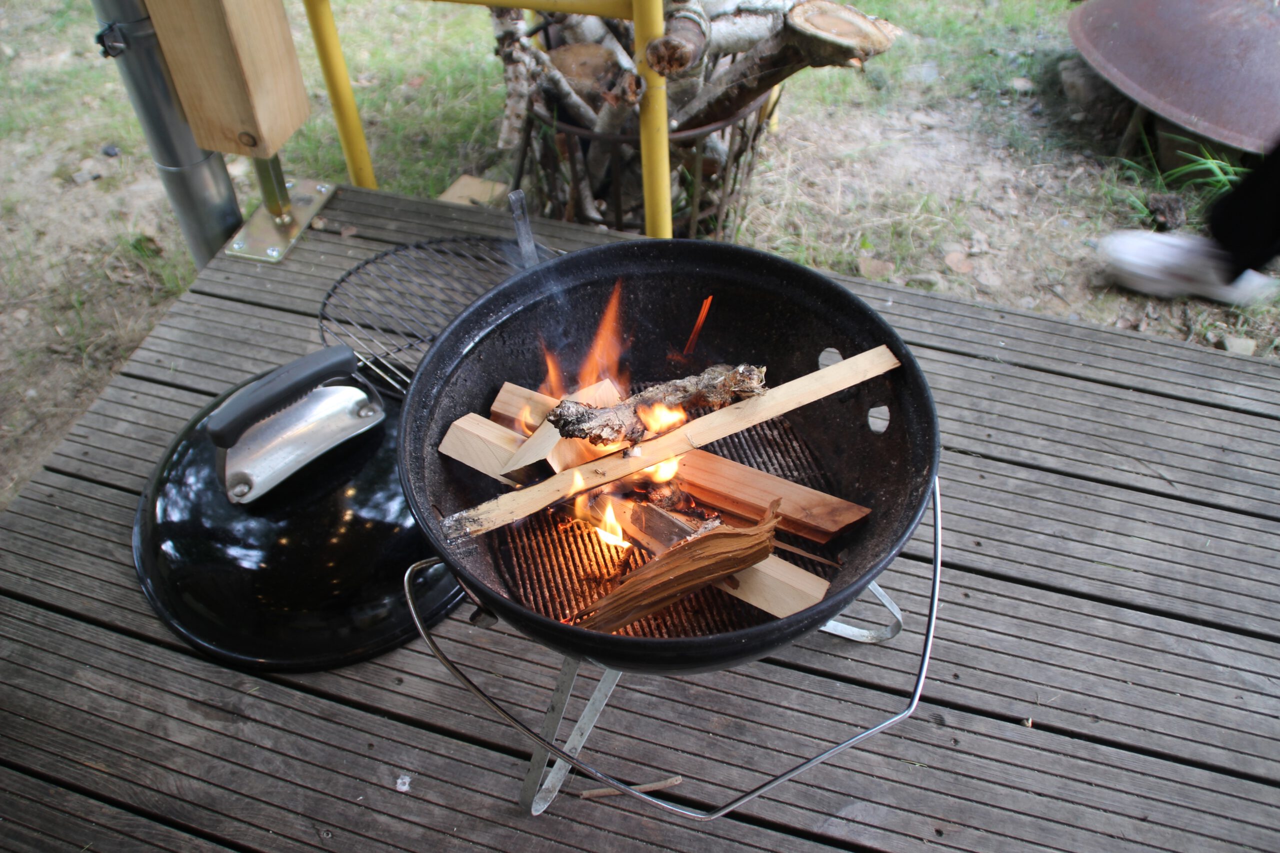 Josephine Caravan Aywaille outdoor barbecue grill with burning wood and charcoal during a relaxed evening on the wooden terrace