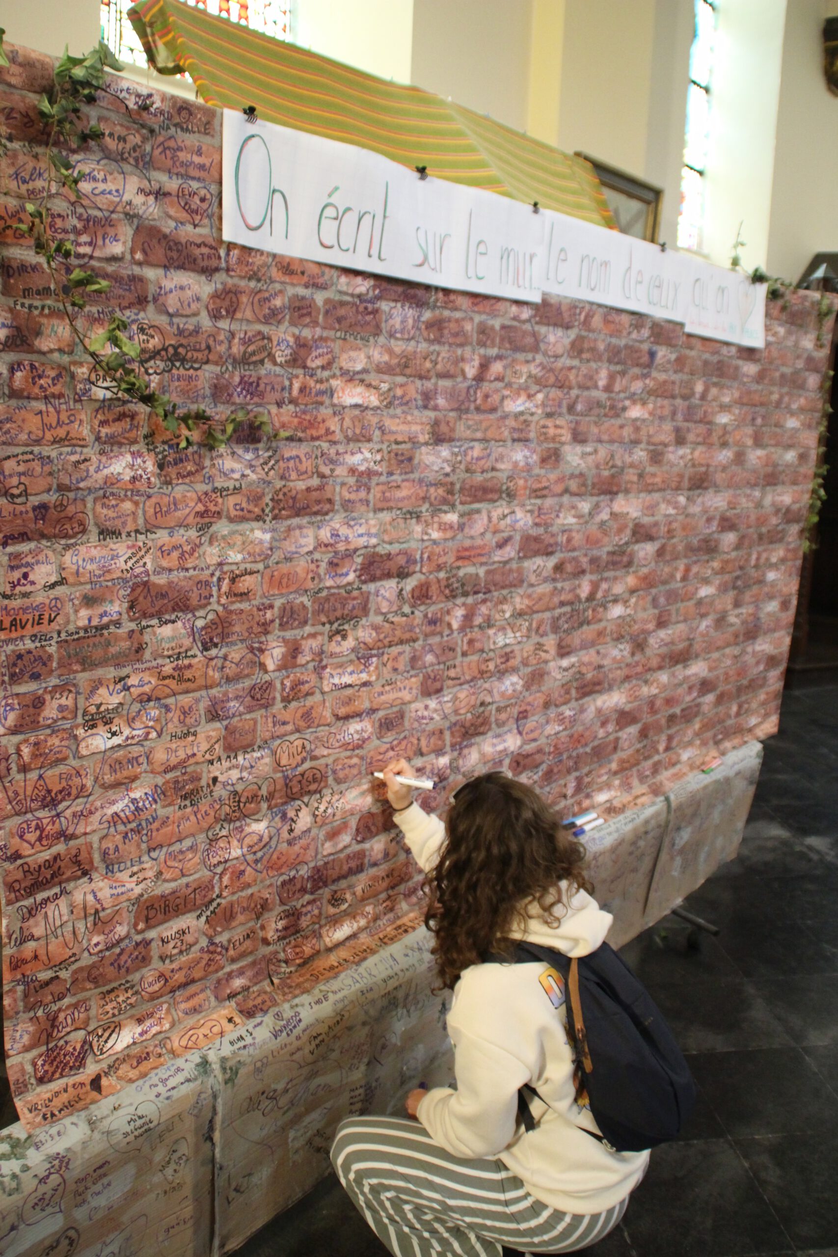 Saint Remaclus Church in Spa interior, visitor writing a name on the symbolic brick wall inside the Roman Catholic church in Spa, Belgium