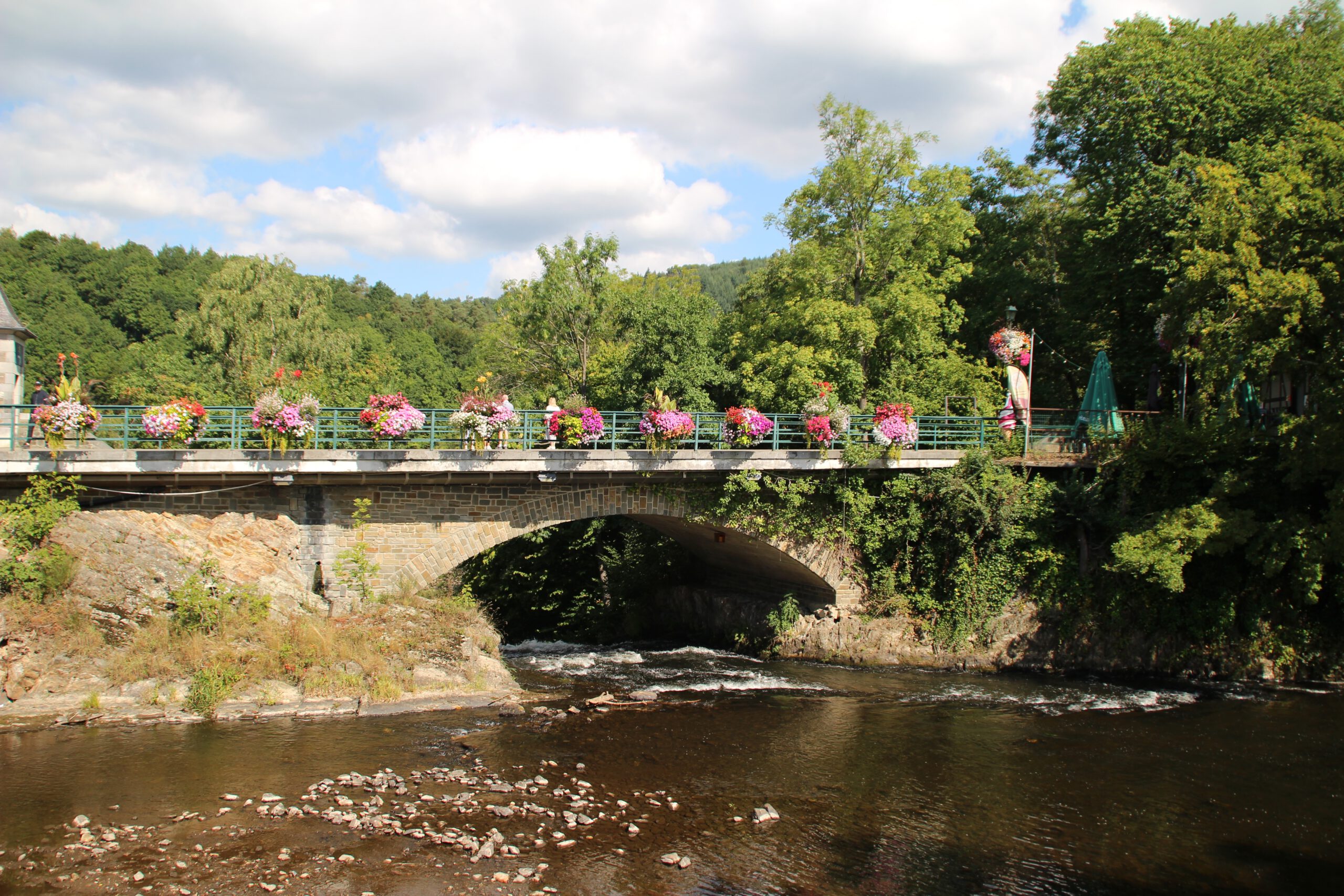 Watervallen of Coo stone bridge over the Amblève River, scenic view of the historic bridge with colorful flowers surrounded by forest in Coo, Belgian Ardennes