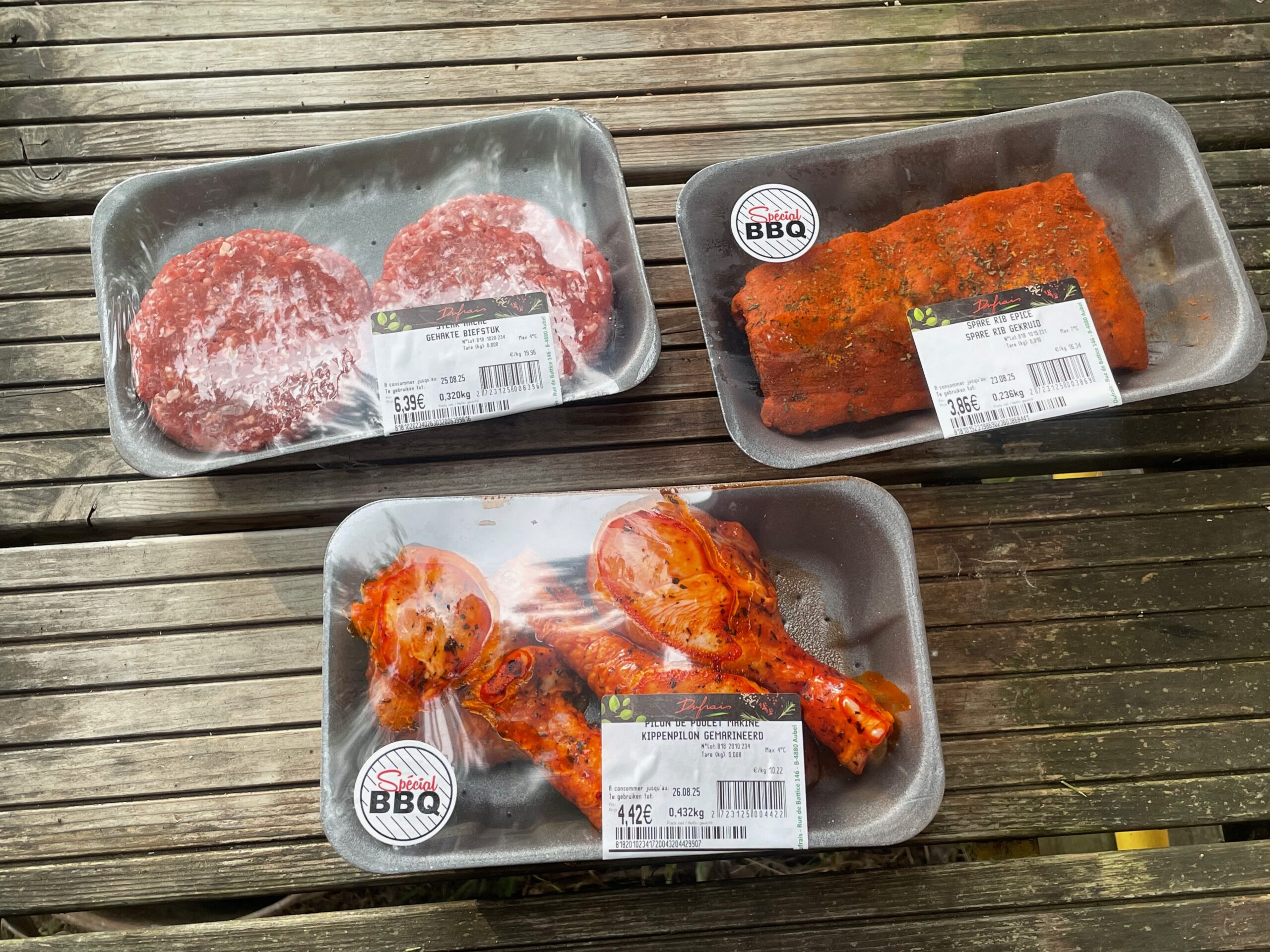 Josephine Caravan Aywaille barbecue night ingredients with fresh beef burgers, marinated ribs, and chicken prepared for outdoor grilling, bought at the Carrefour Market in town