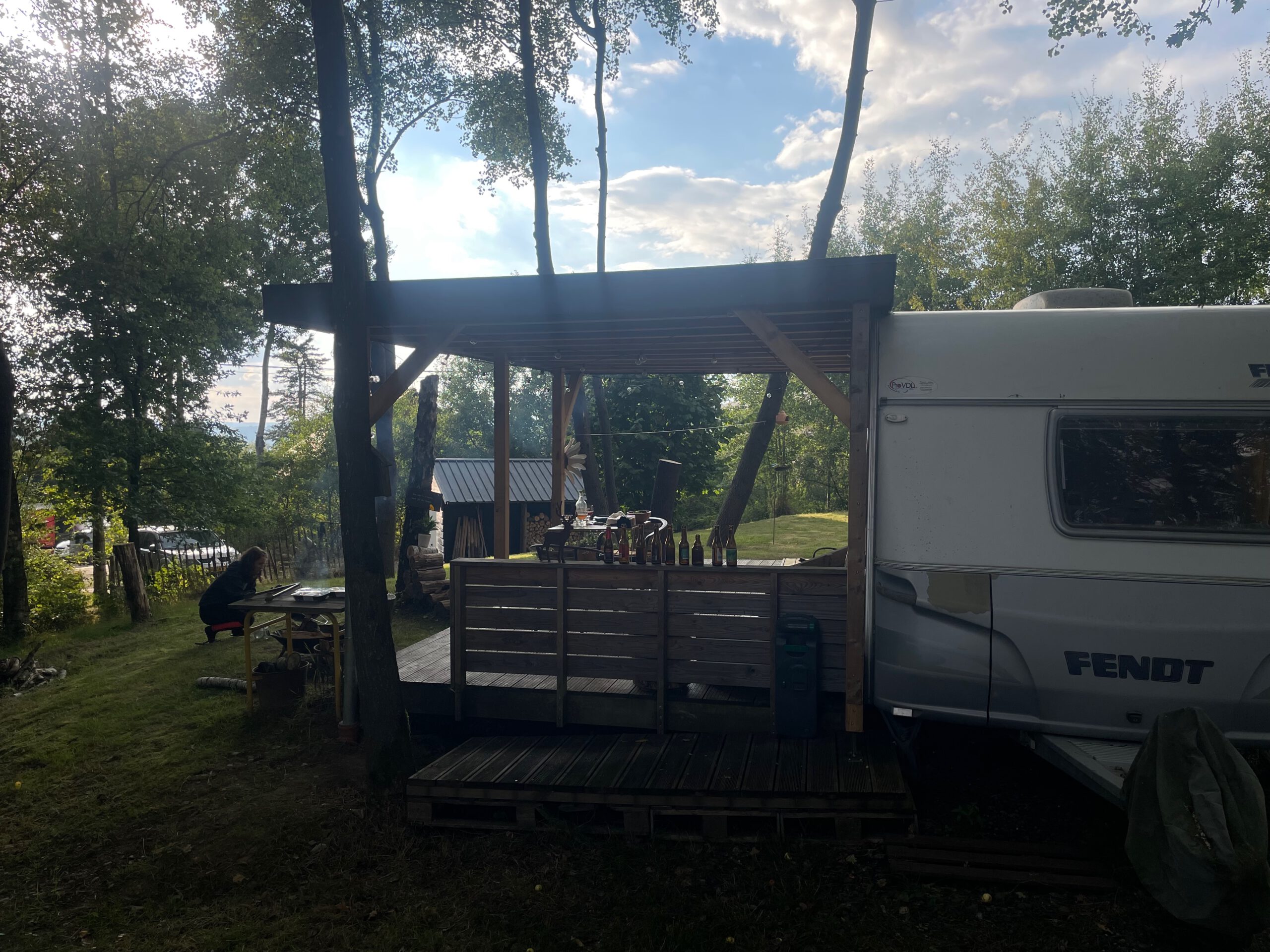 Josephine Caravan Aywaille outdoor covered terrace with barbecue area, firewood, and forest setting in the Belgian Ardennes