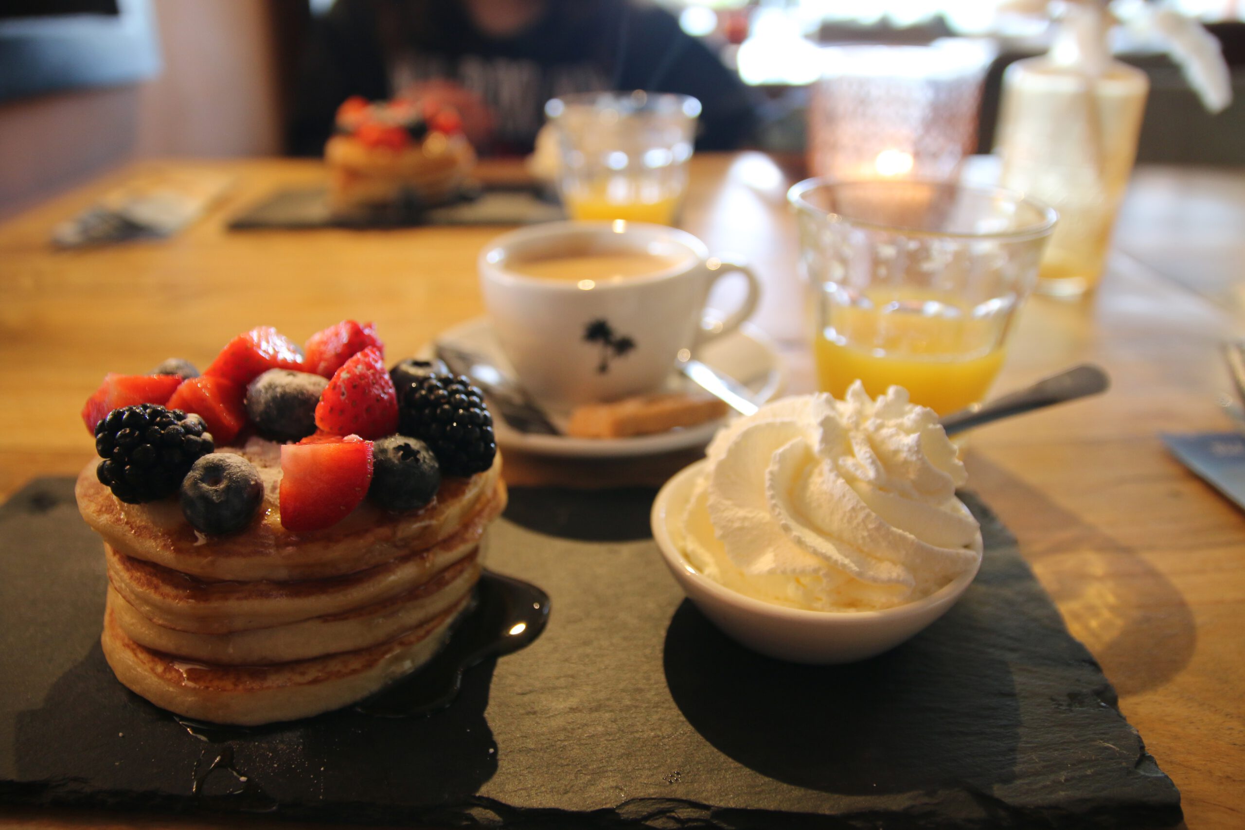 American pancakes breakfast at Strandrestaurant Nederzandt Noordwijk with fresh berries, whipped cream, coffee, and fresh orange juice on a wooden table