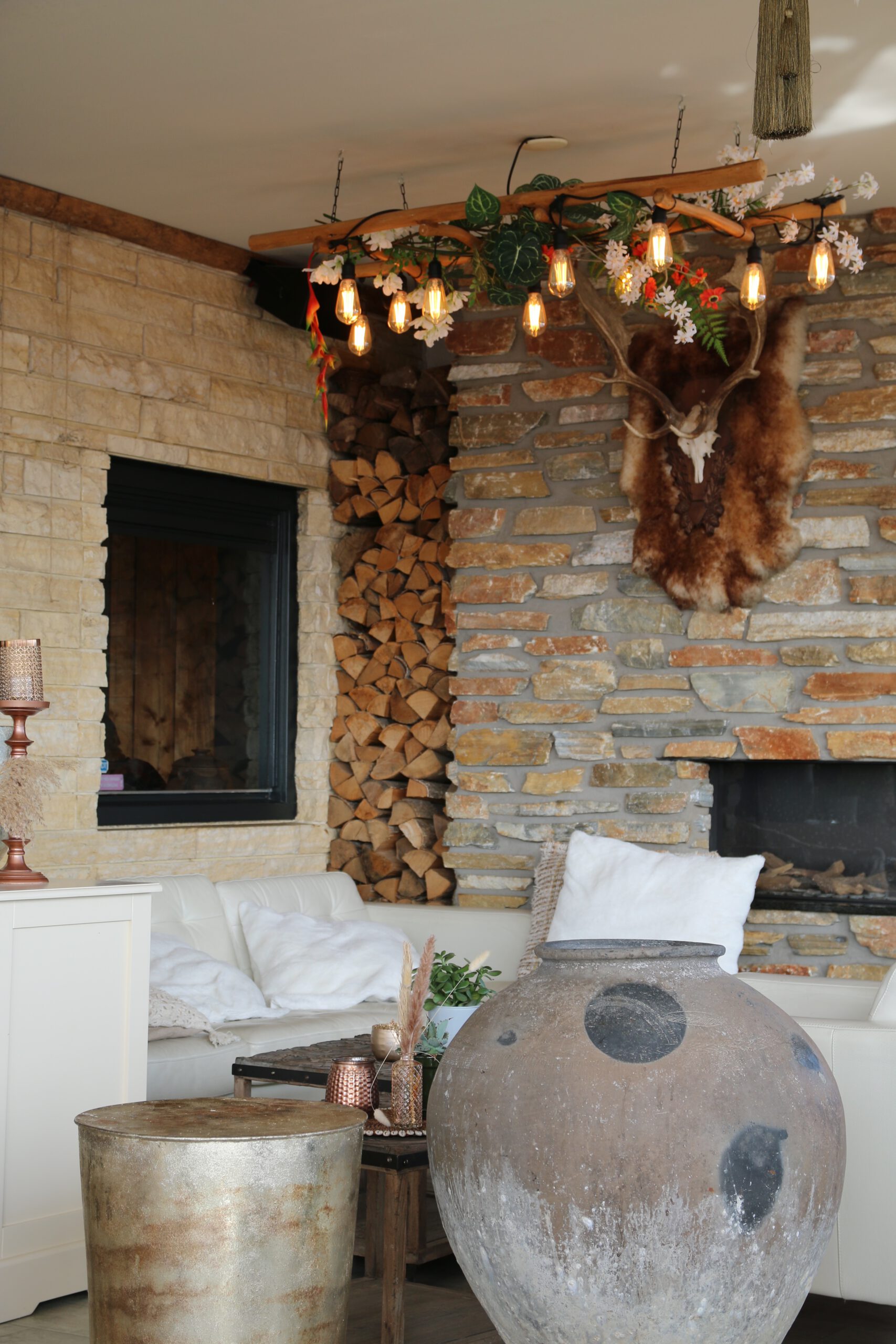 Cozy interior atmosphere at Strandrestaurant Nederzandt Noordwijk with natural stone walls, stacked firewood, warm lighting and a relaxed beach lounge setting