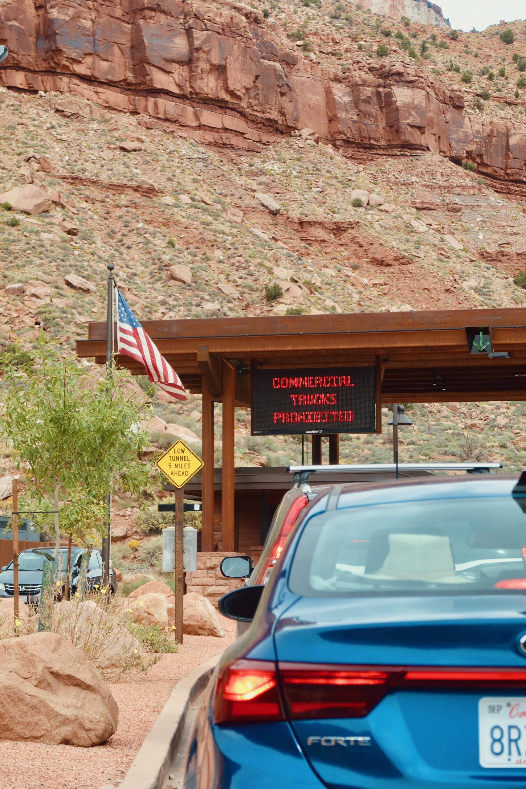 Vehicles waiting near the Zion Mount Carmel Tunnel entrance with National Park Service signage and red rock canyon walls