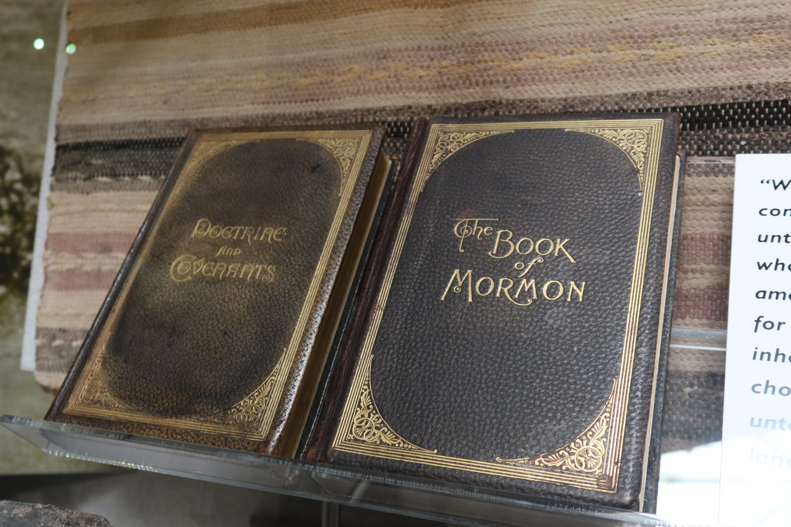 Historic editions of The Book of Mormon and Doctrine and Covenants displayed behind glass, featuring dark leather covers with gold lettering