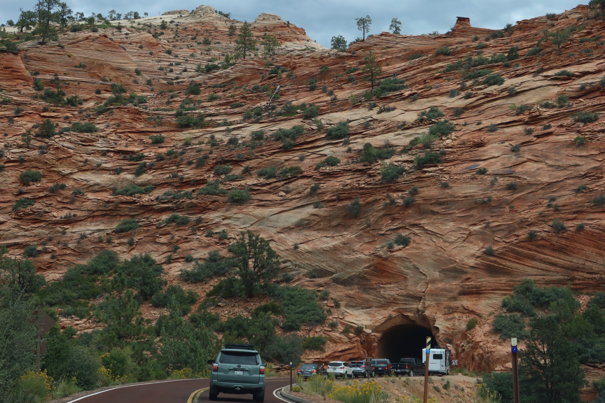 Traffic approaching the Zion Mount Carmel Tunnel, surrounded by layered red sandstone cliffs in Zion National Park, Utah