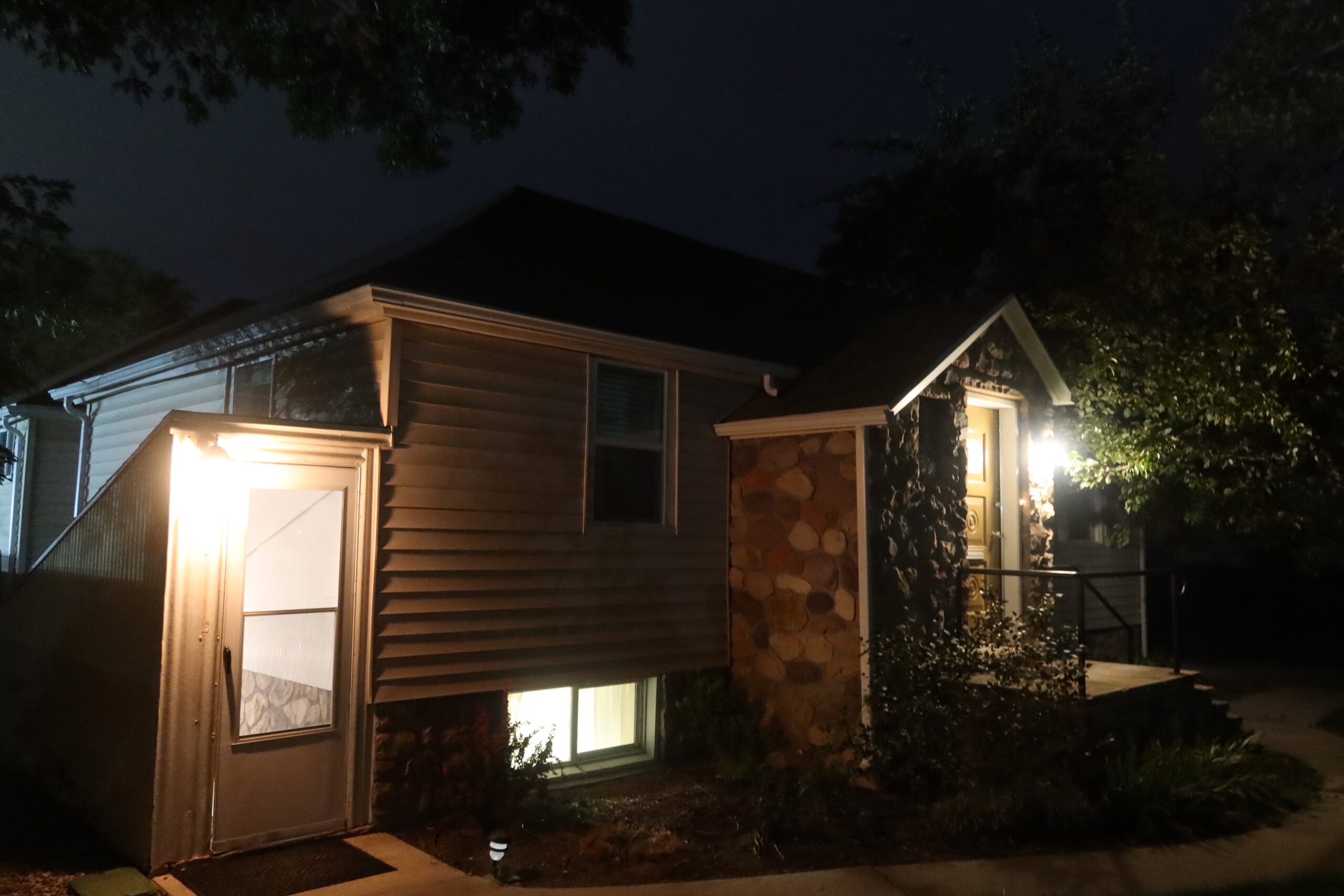Exterior view of a Sandy Utah Airbnb basement entrance at night, featuring a private entrance with outdoor lighting, stone details, and ground level windows, perfect for a quiet Utah road trip stay