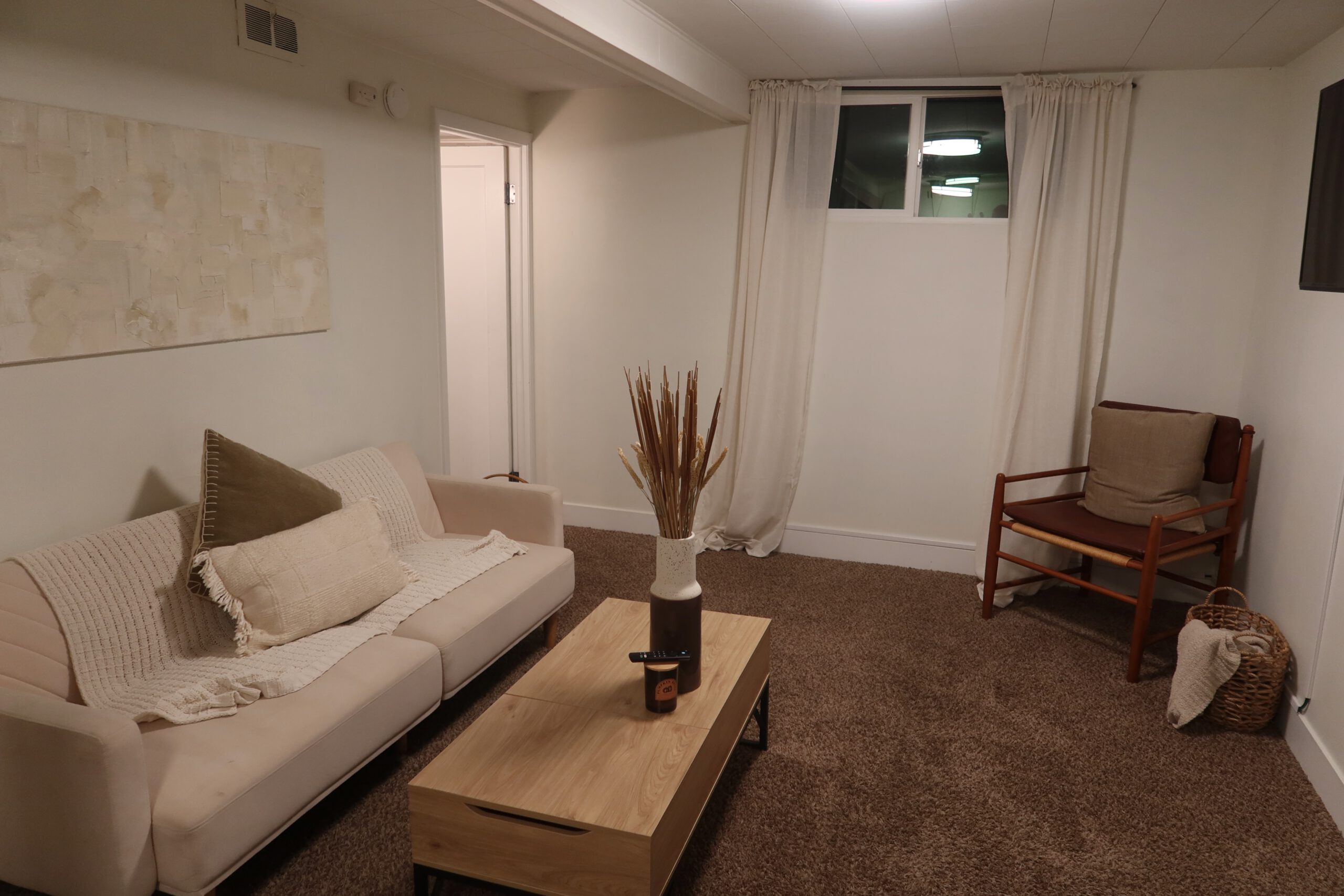 Cozy living area in a Sandy Utah Airbnb basement stay, featuring a comfortable sofa, coffee table, reading chair, soft lighting, and minimalist decor, perfect for relaxing after a Utah road trip