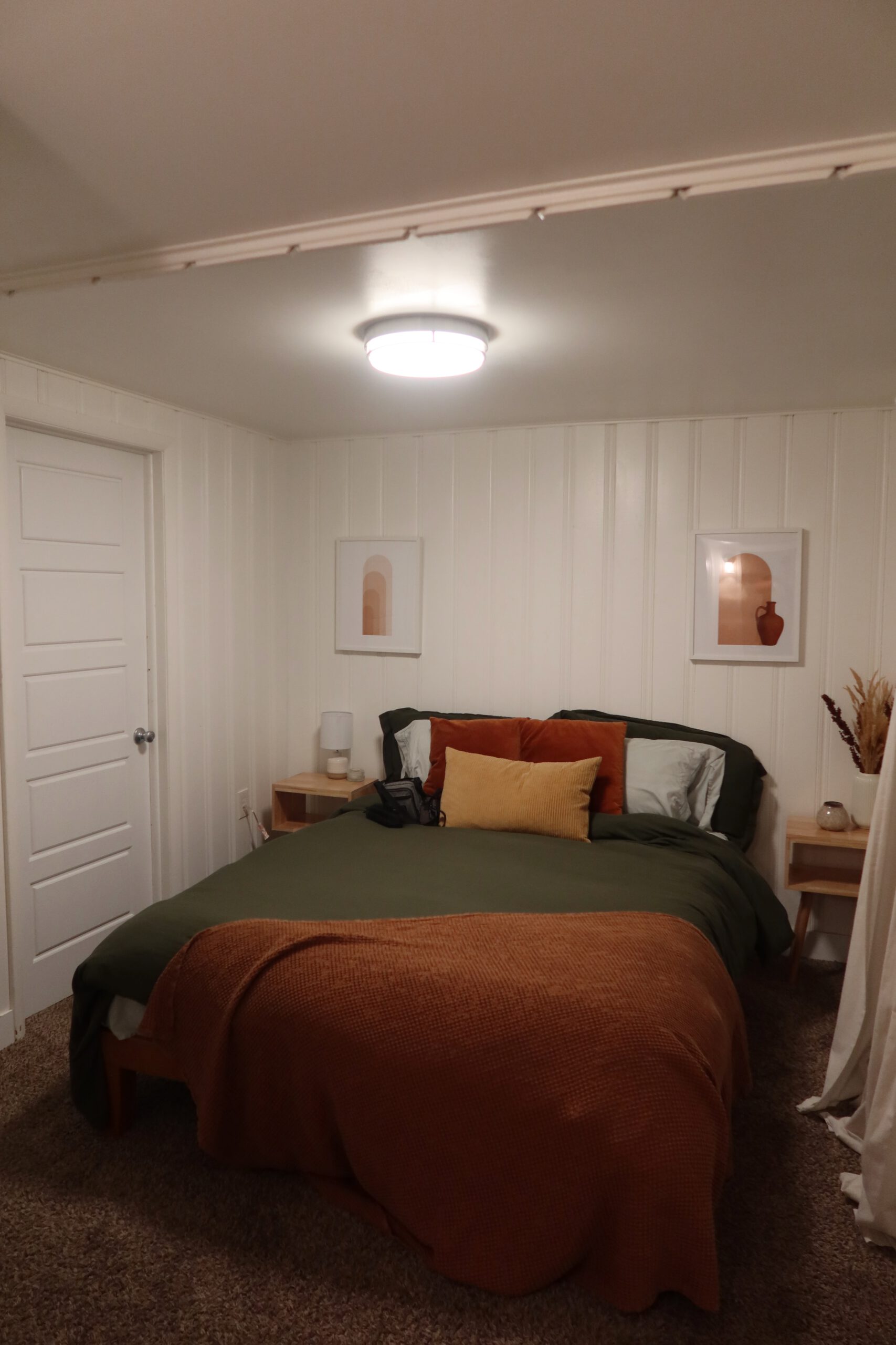 Cozy bedroom in a Sandy Utah Airbnb basement stay, featuring a queen size bed with warm earth tone bedding, bedside tables, soft lighting, and minimalist decor, ideal for a relaxing Utah road trip stop