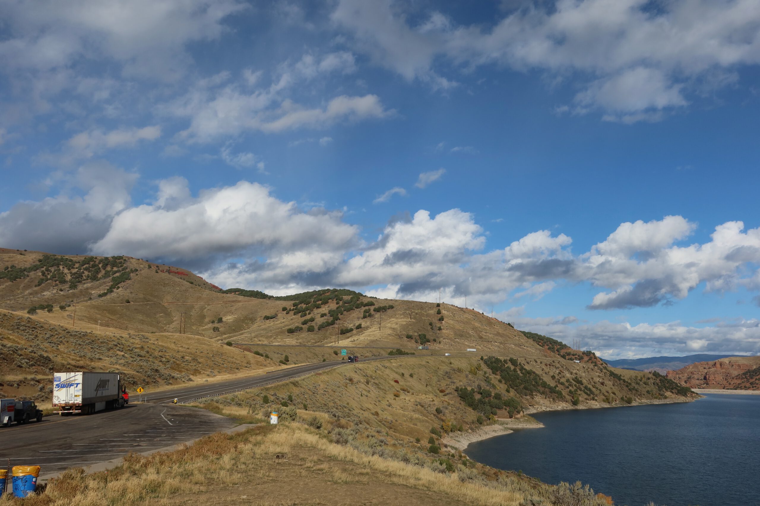 Wide view of Echo Reservoir near Coalville Utah, showing deep blue water, dry golden hills, and scattered clouds, photographed from a roadside viewing point along Interstate 80.