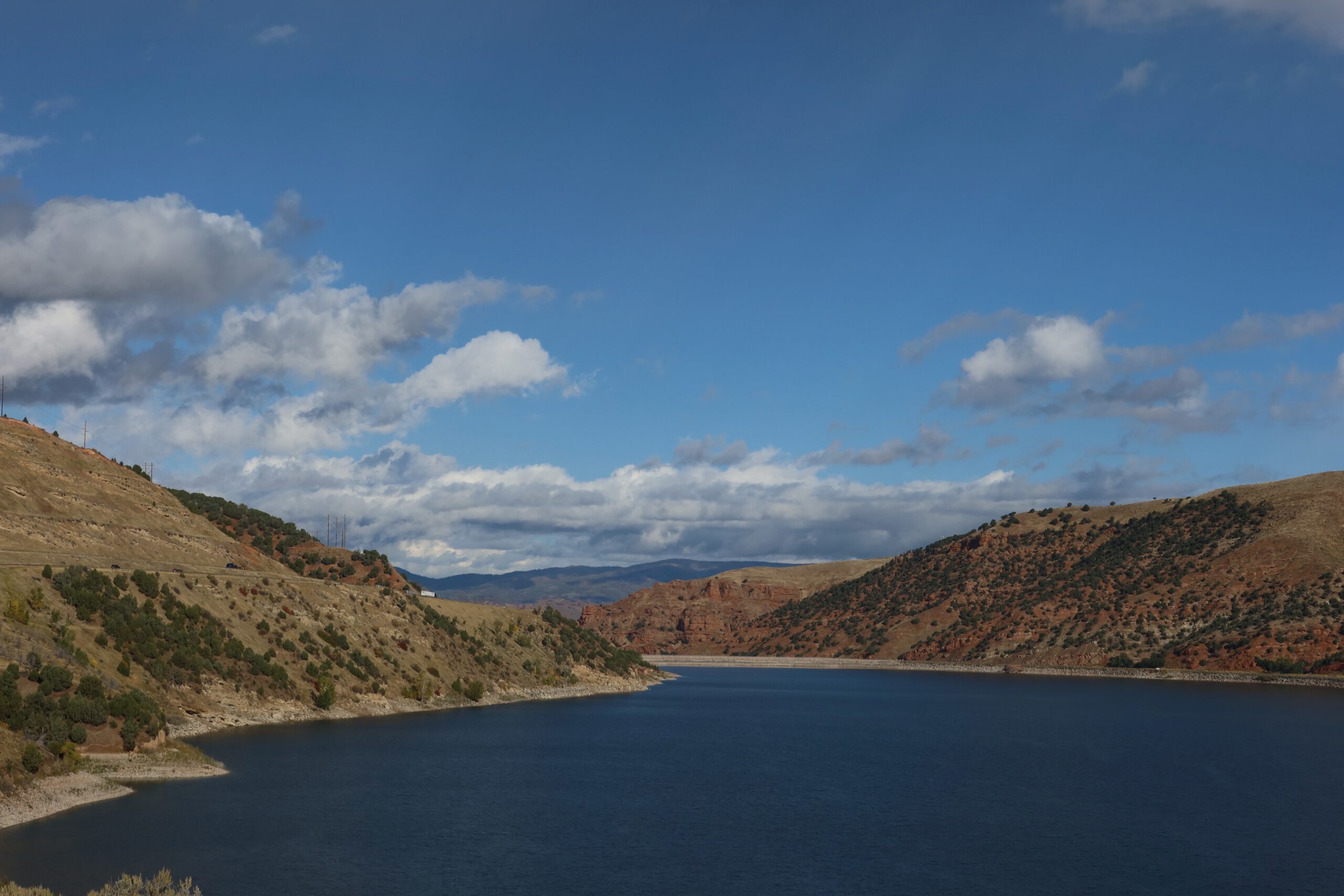 Scenic view of Echo Reservoir near Coalville Utah, with calm blue water framed by rolling hills and distant red rock formations under a wide open sky, captured during a Utah road trip stop.